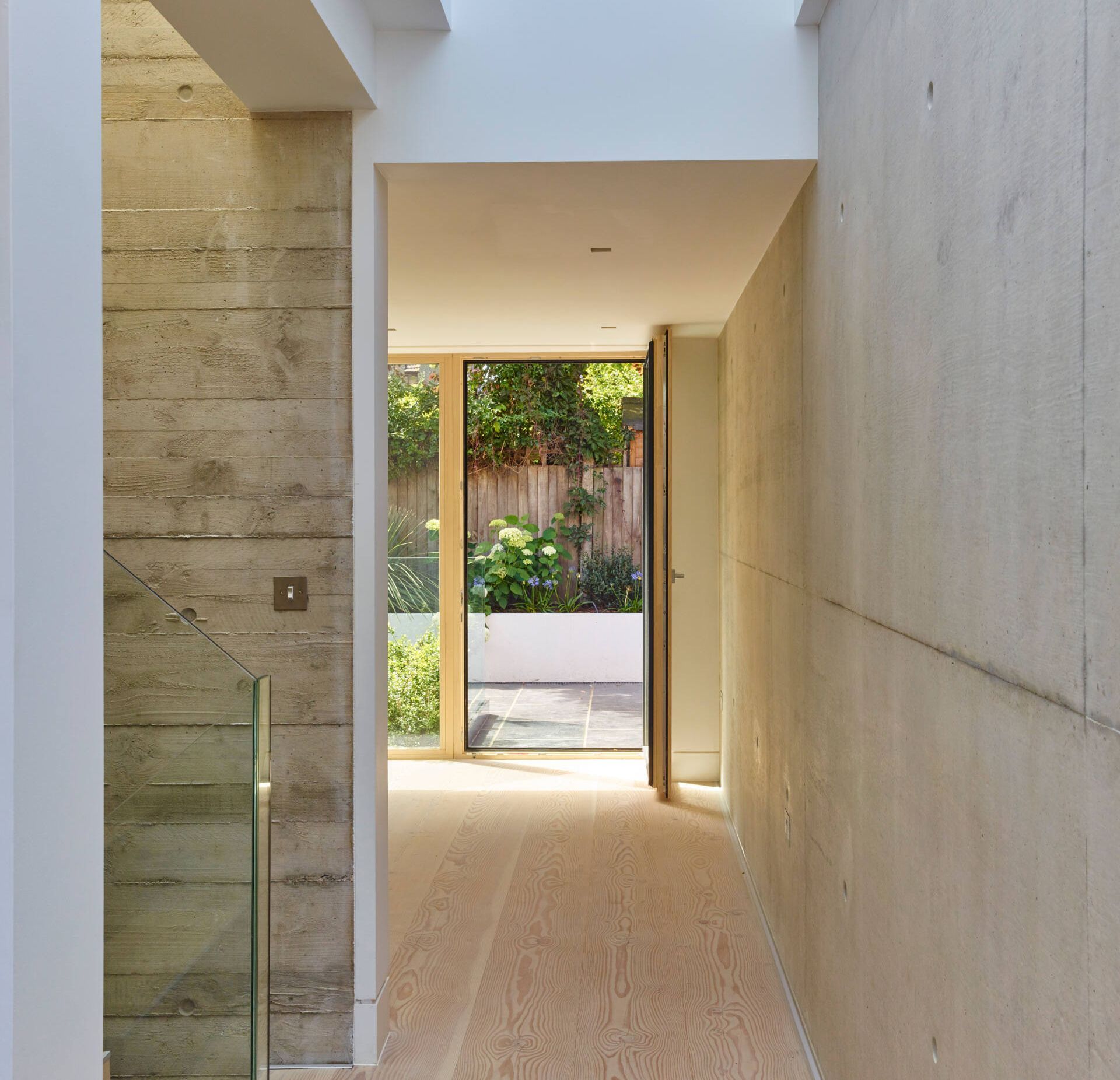 Modern narrow hallway with stone and white walls, leading to a sunlit courtyard garden.