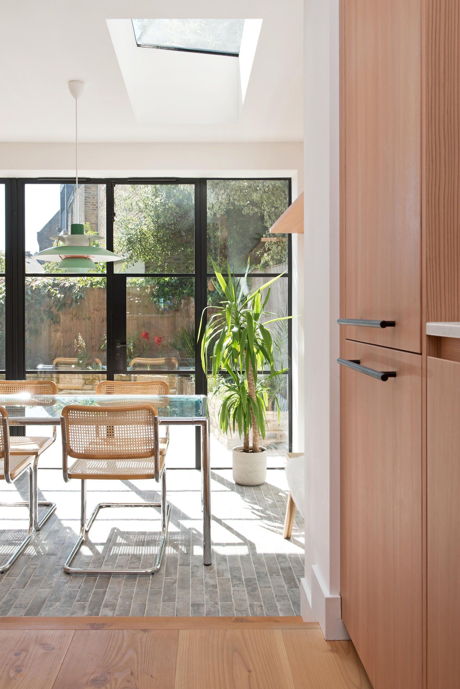 Sunlit dining area with glass doors, wooden table, chair, plant, and skylight.