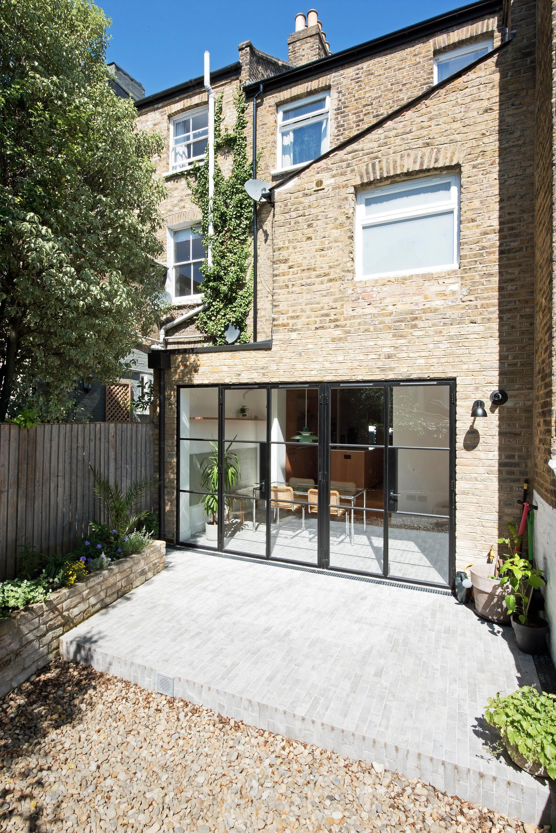 Rear brick townhouse with a modern glass rear extension and paved patio in a small garden