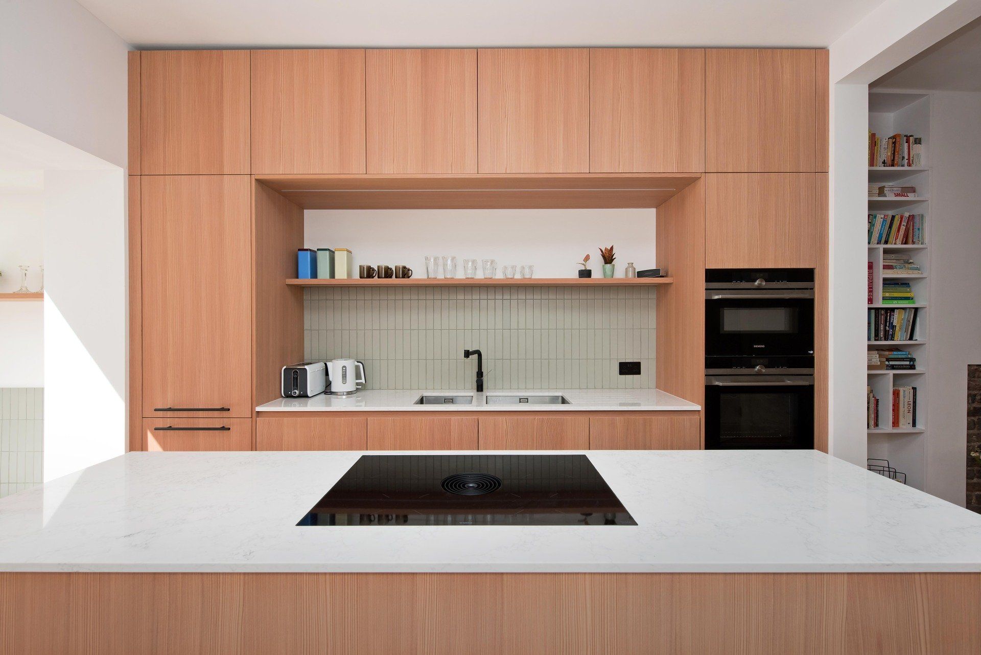 Modern kitchen with wood cabinetry, white island countertop, and built-in appliances
