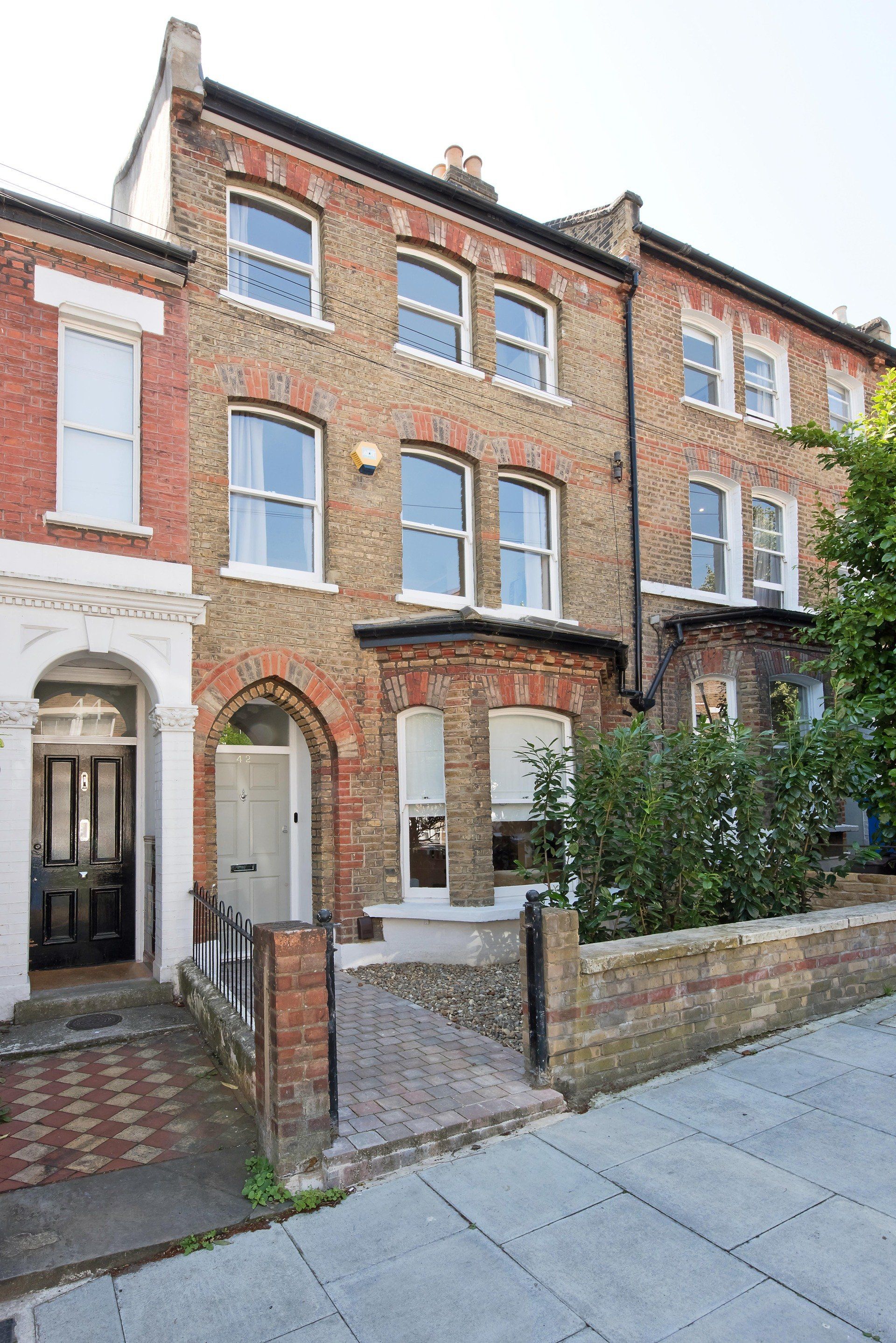 Row of red-brick terraced houses with a small front garden and paved sidewalk.