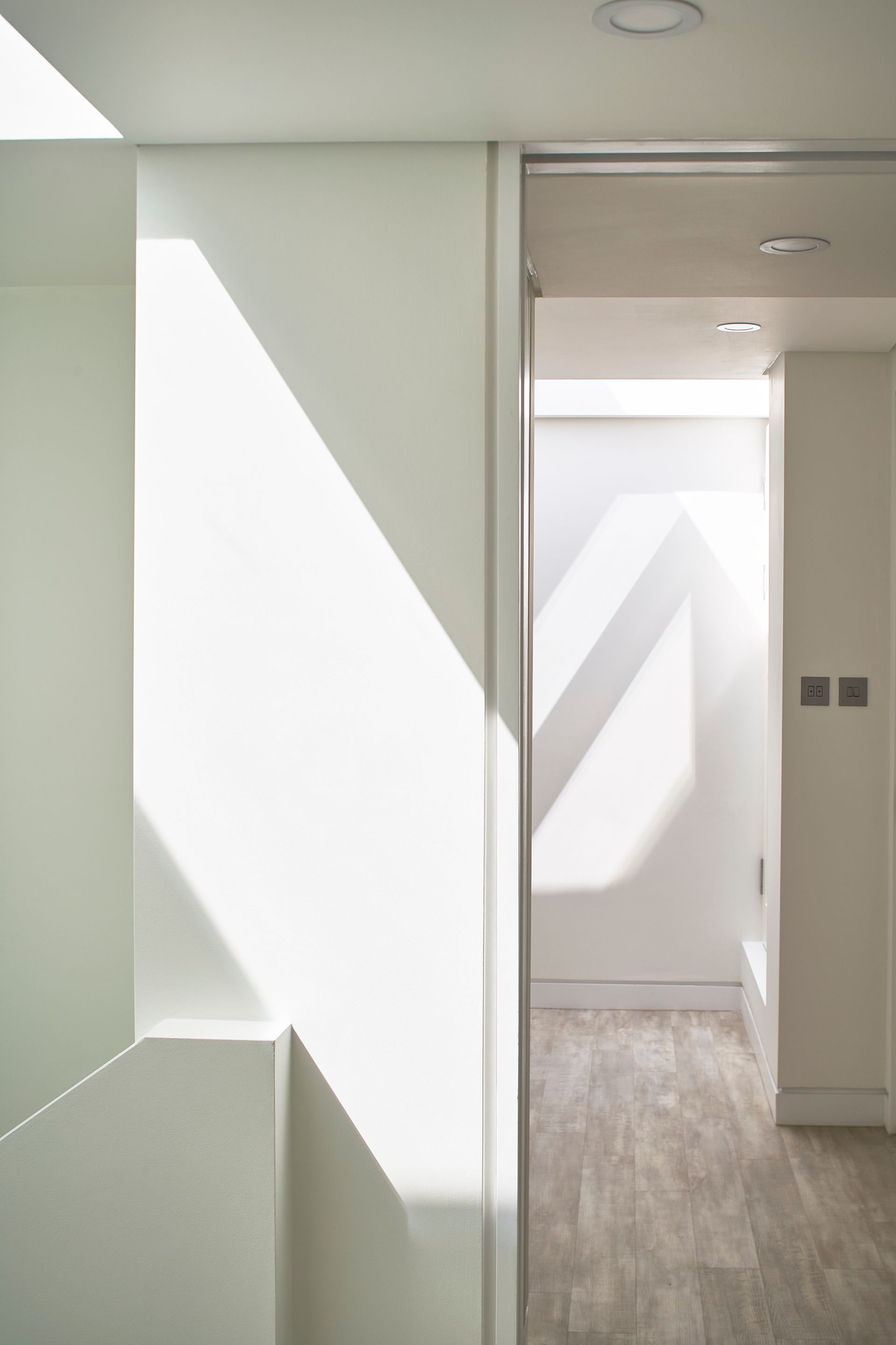 Bright hallway with white walls, soft sunlight, and an open doorway leading to another room