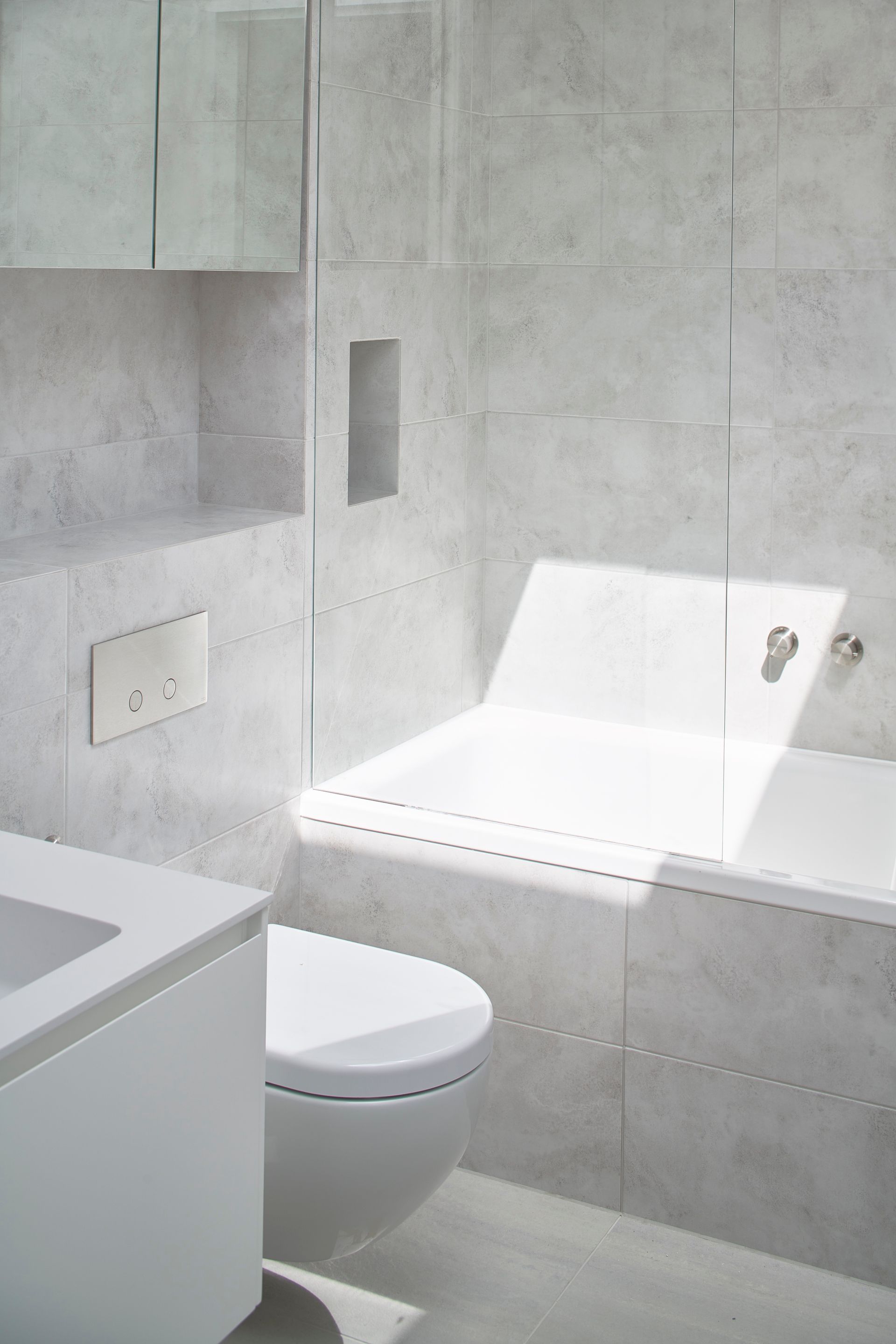 Modern gray-tiled bathroom with toilet, sink, built-in tub, and wall mirror