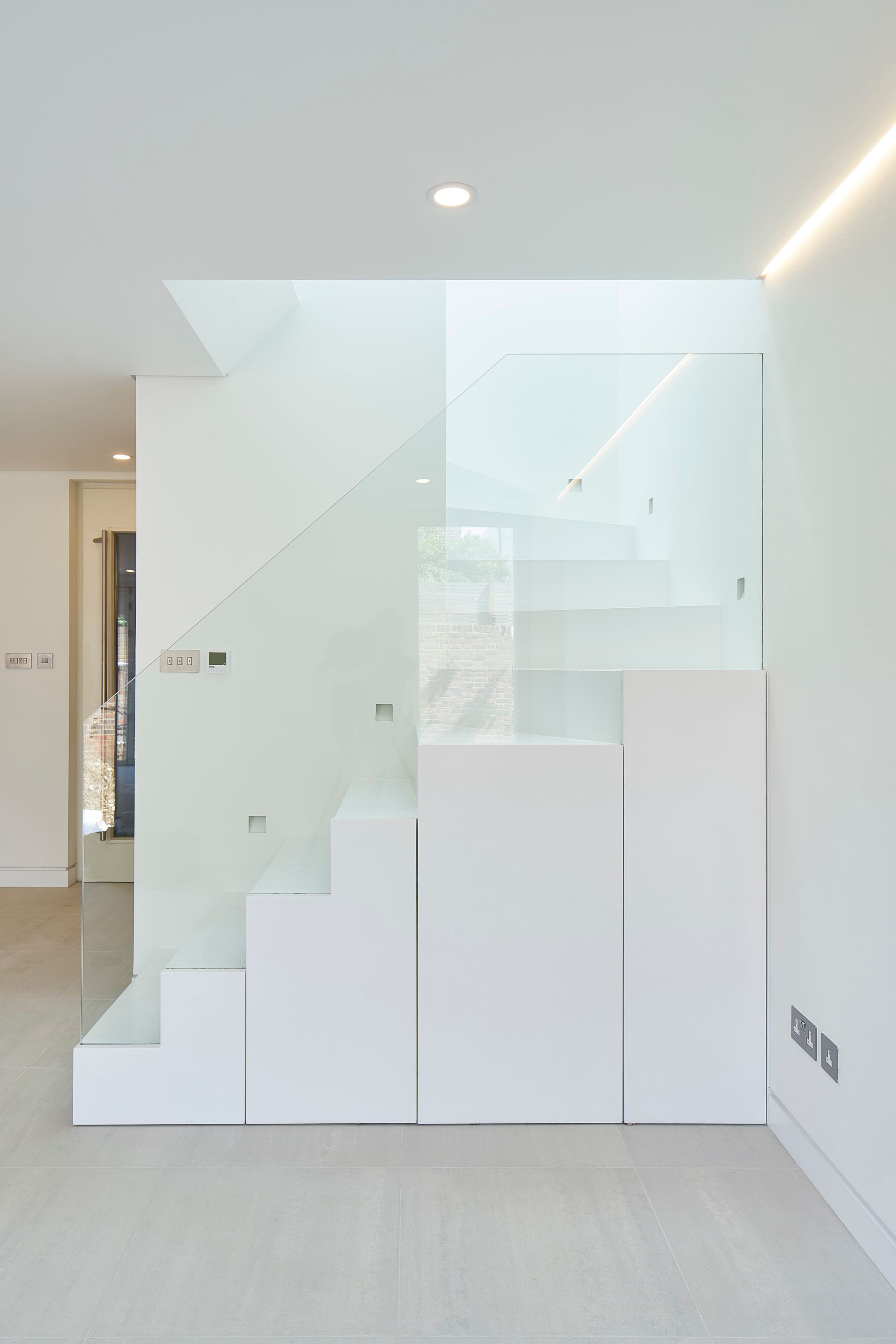 Minimalist stairway with white steps, glass railing, and bright modern interior.