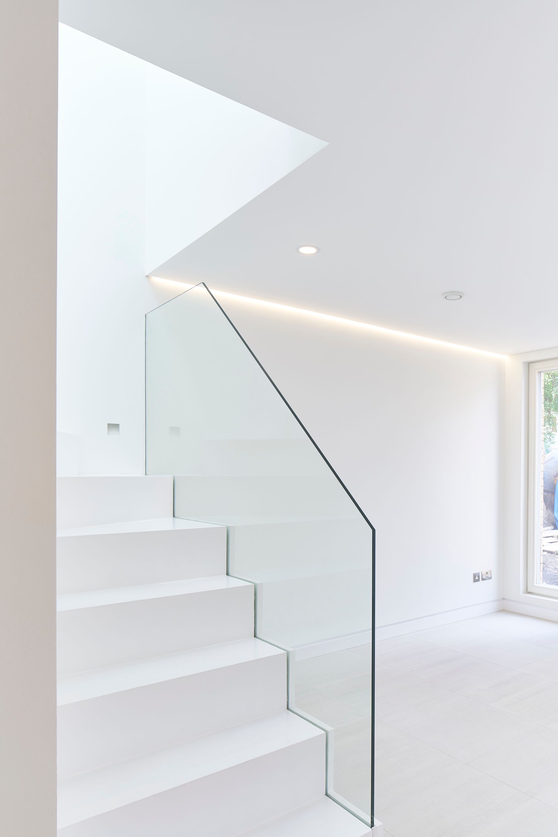 Minimal white staircase with glass railing in a bright modern interior