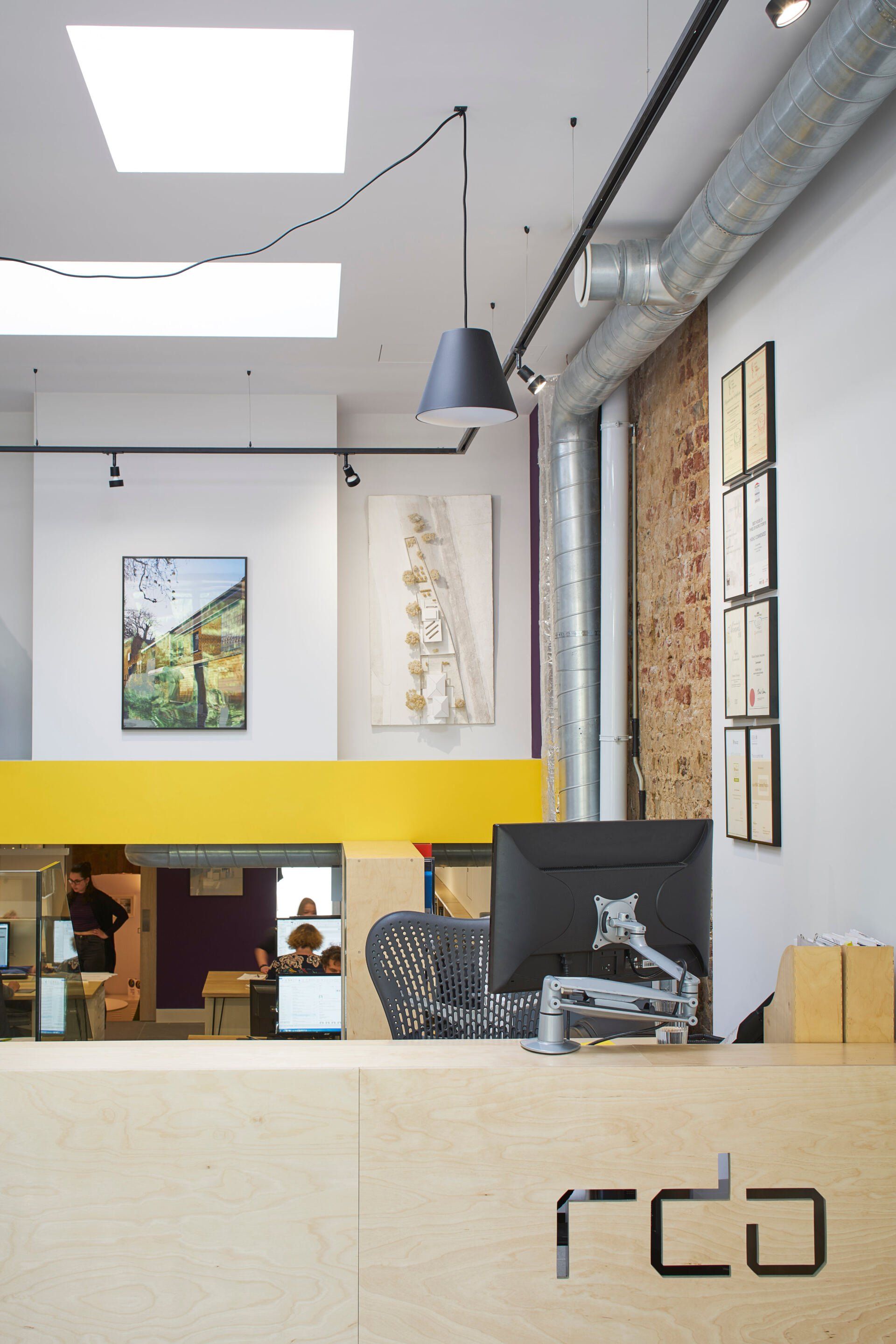Modern office lobby with a reception desk, yellow accent wall, and hanging pendant lights