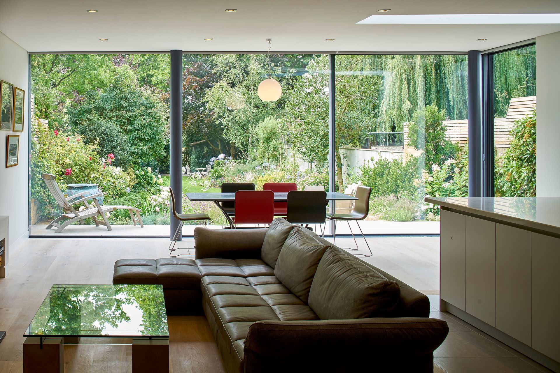Modern living room with sofa, glass coffee table, and large sliding doors opening to a green garden.
