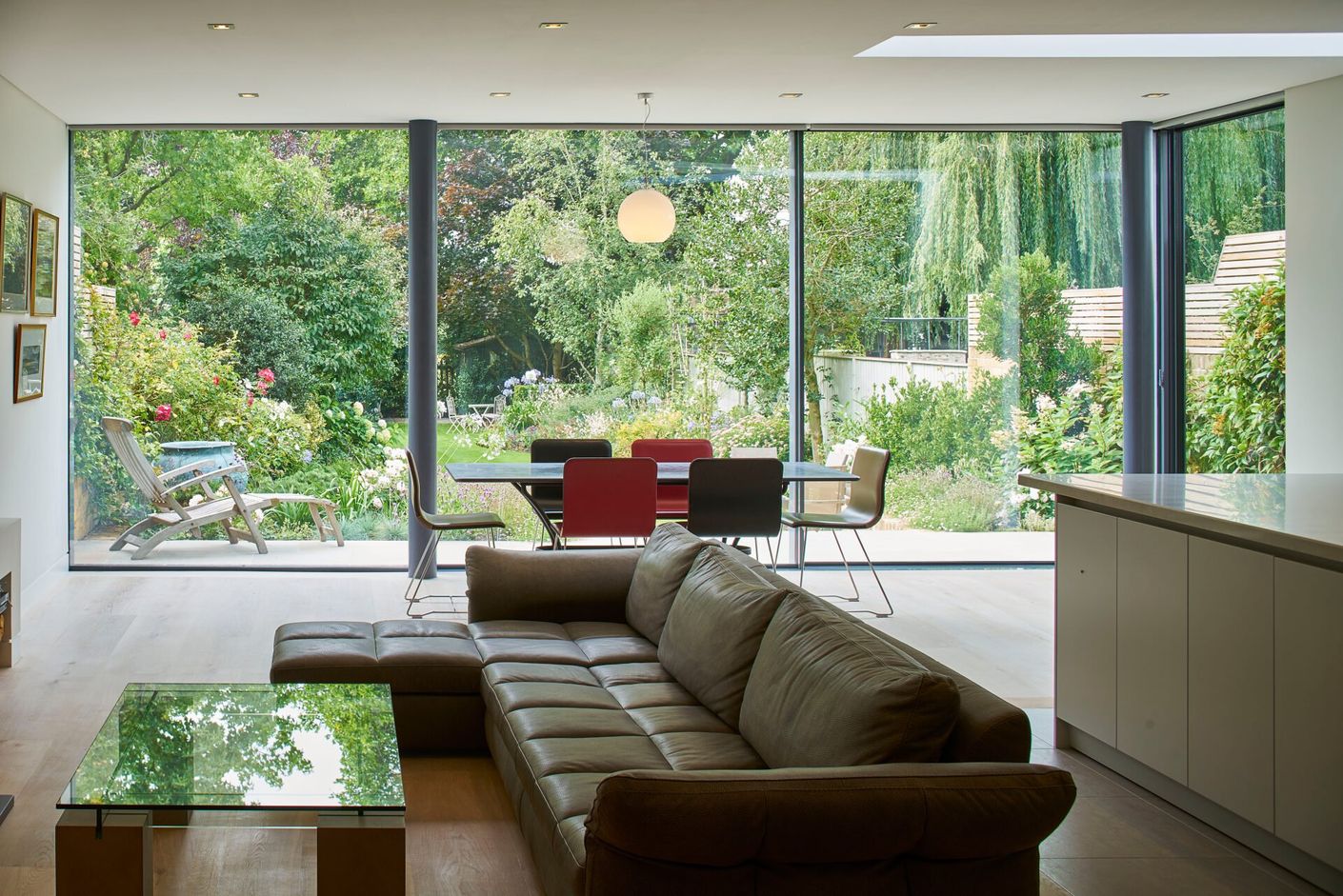 Modern living room with sofa and glass walls opening to a green garden