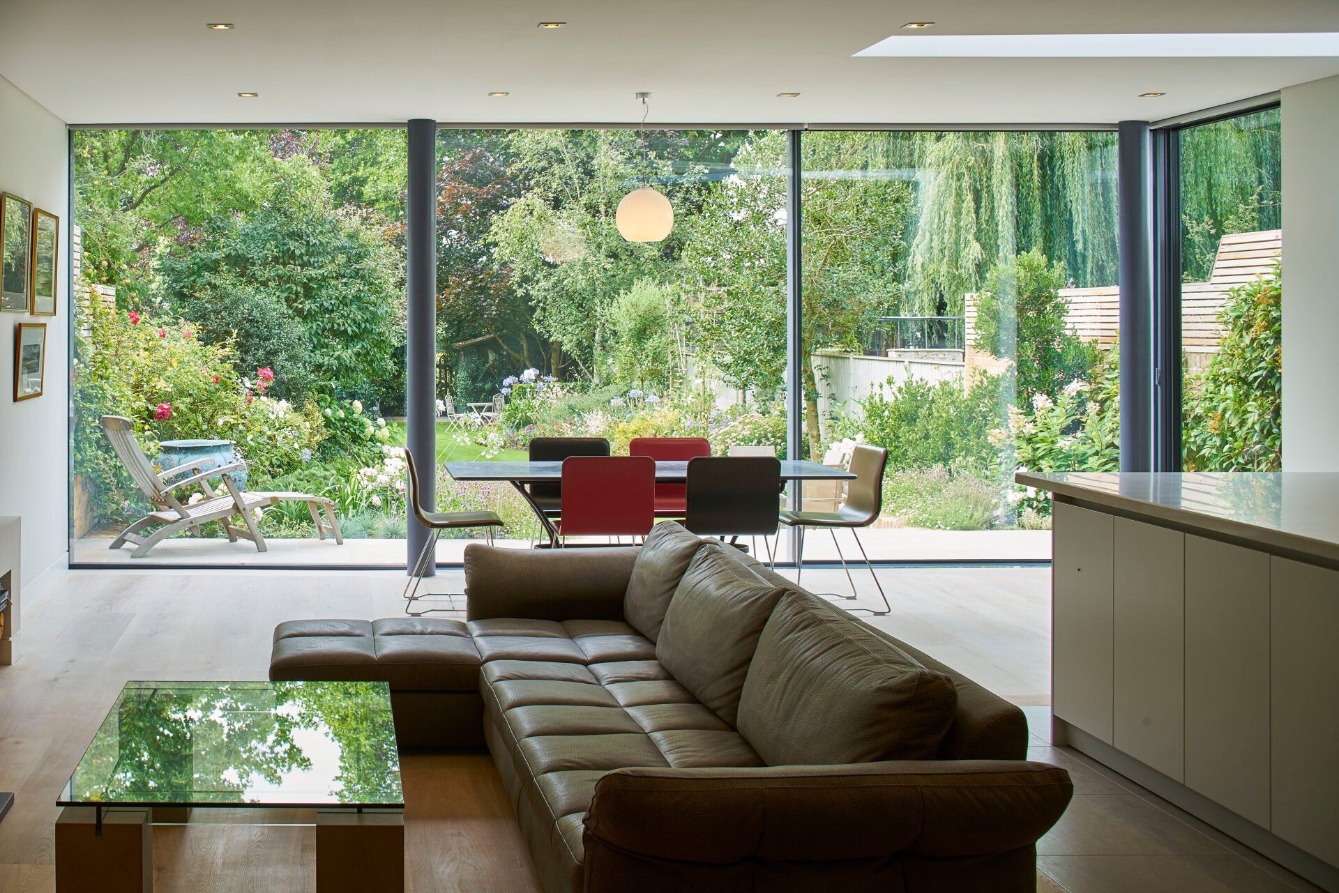 Modern living room with a sofa, glass coffee table, and large windows opening to a green garden.