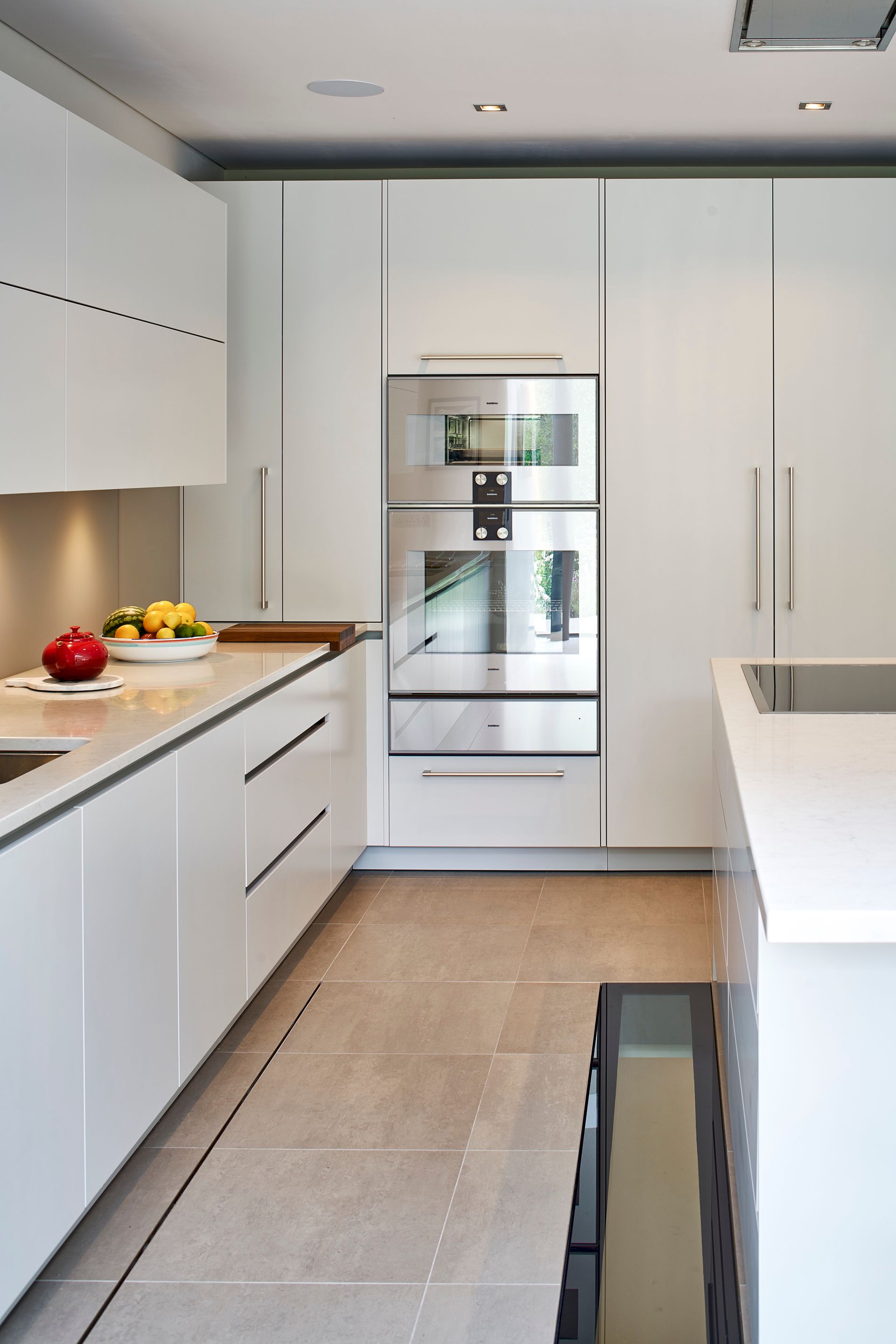 Modern white kitchen with built-in oven, island, and fruit on the counter