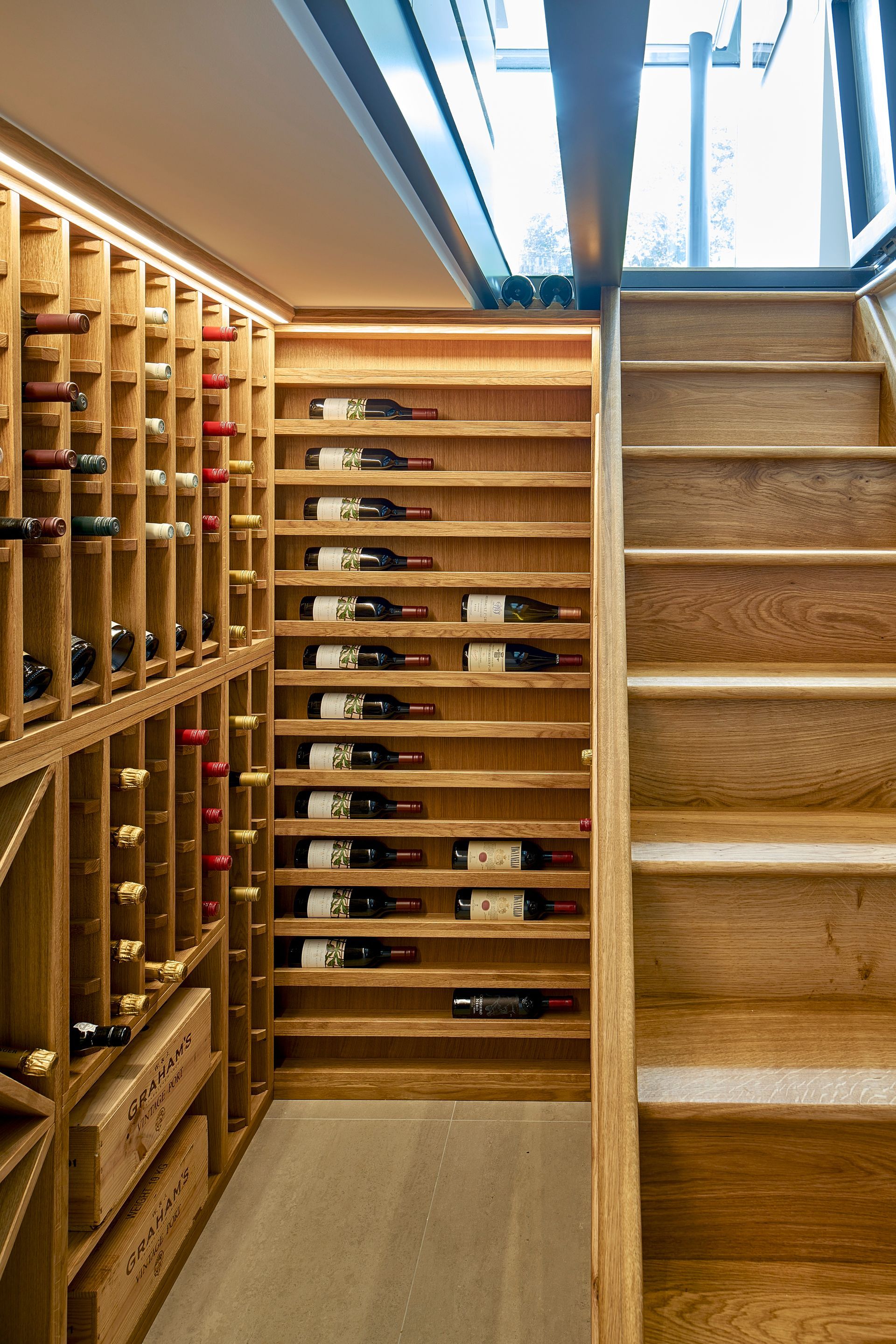 Wine cellar with built-in racks and a carpeted staircase beside a skylit hallway