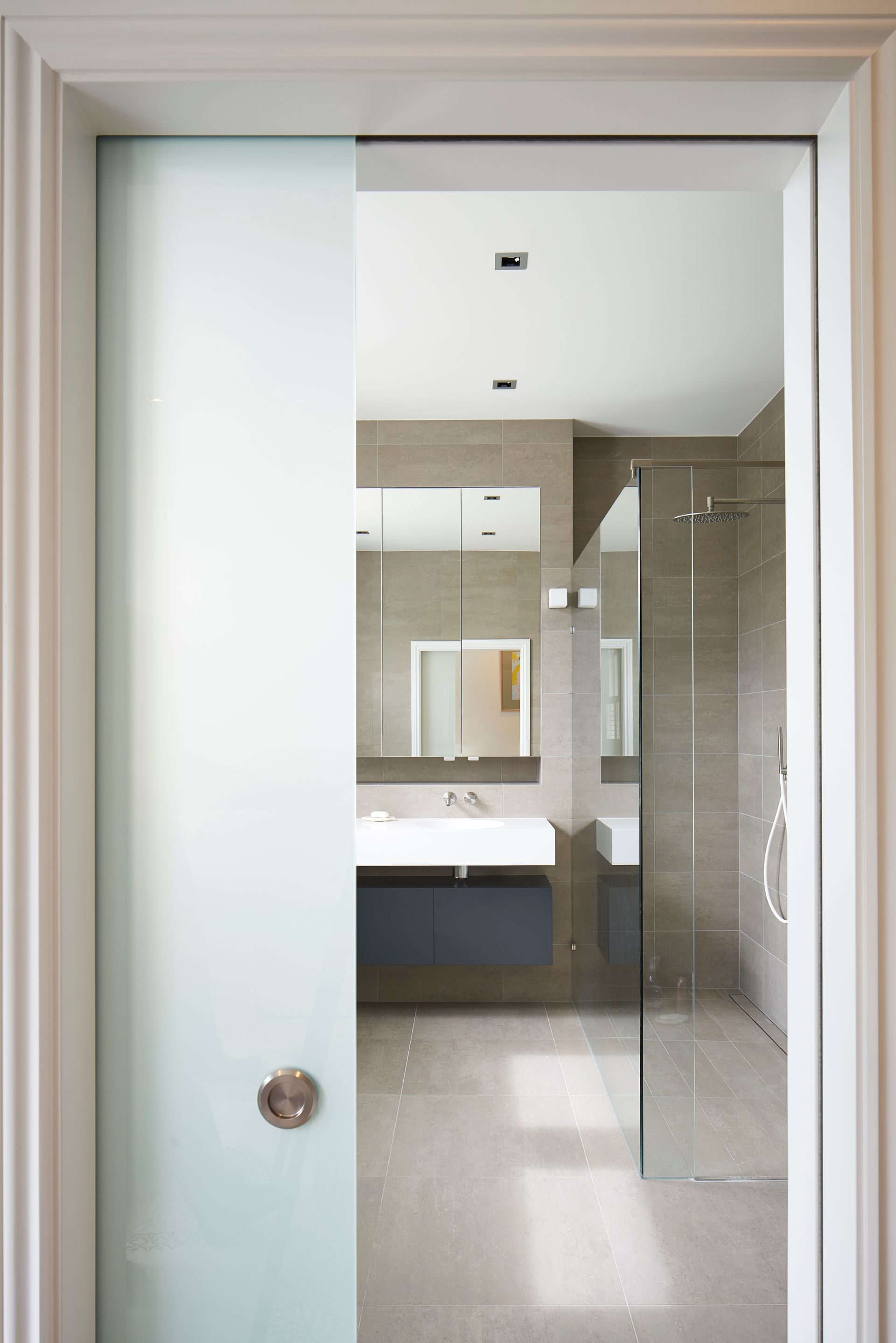 Bathroom with frosted glass door, vanity sink, mirror, and glass shower enclosure.