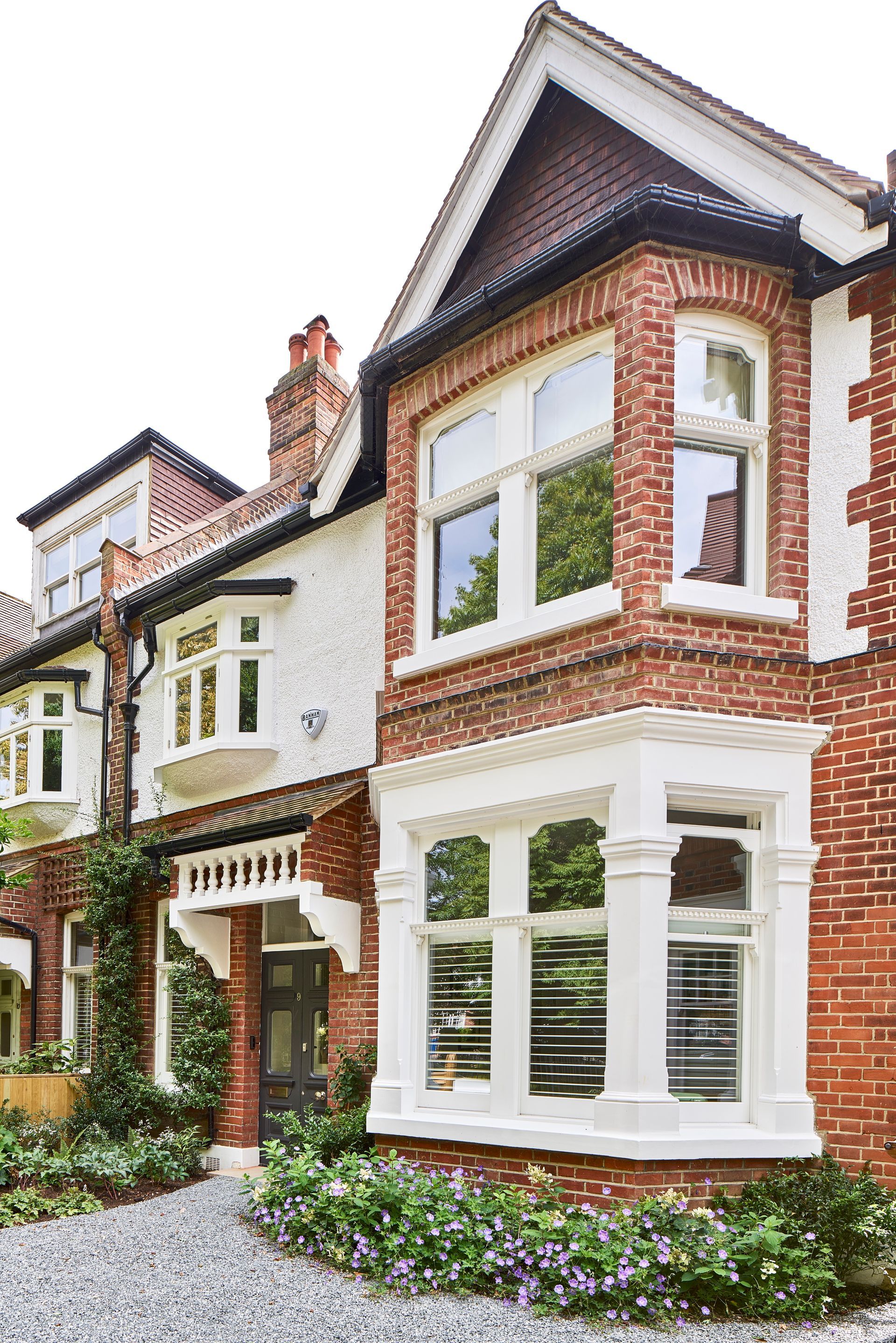 Red-brick Victorian-style house with bay windows and white trim along a gravel driveway