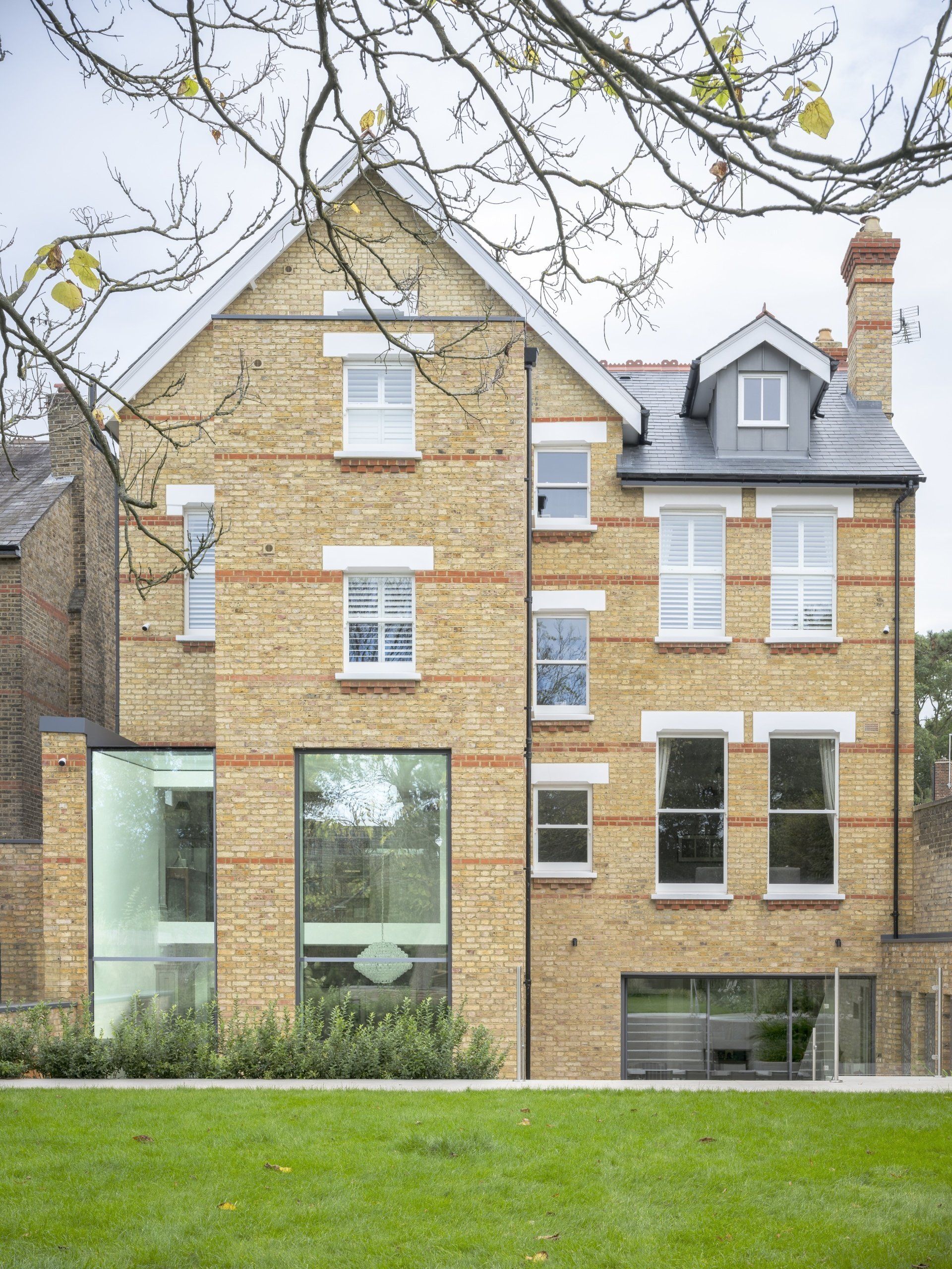 Brick townhouse facade with large windows, a gray roof, and a small lawn in front