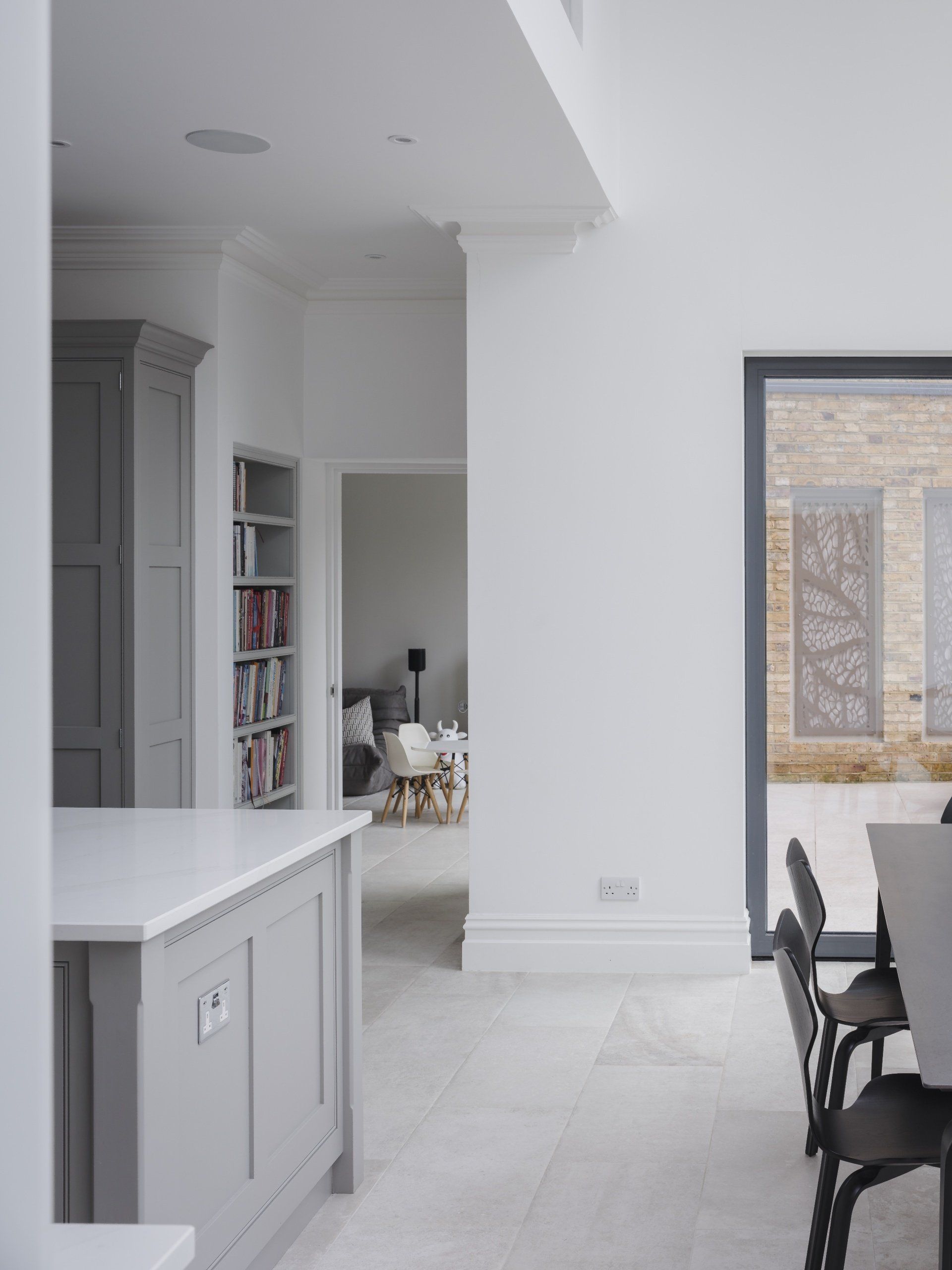 Modern white kitchen with island, gray cabinetry, and a dining area by a large window.