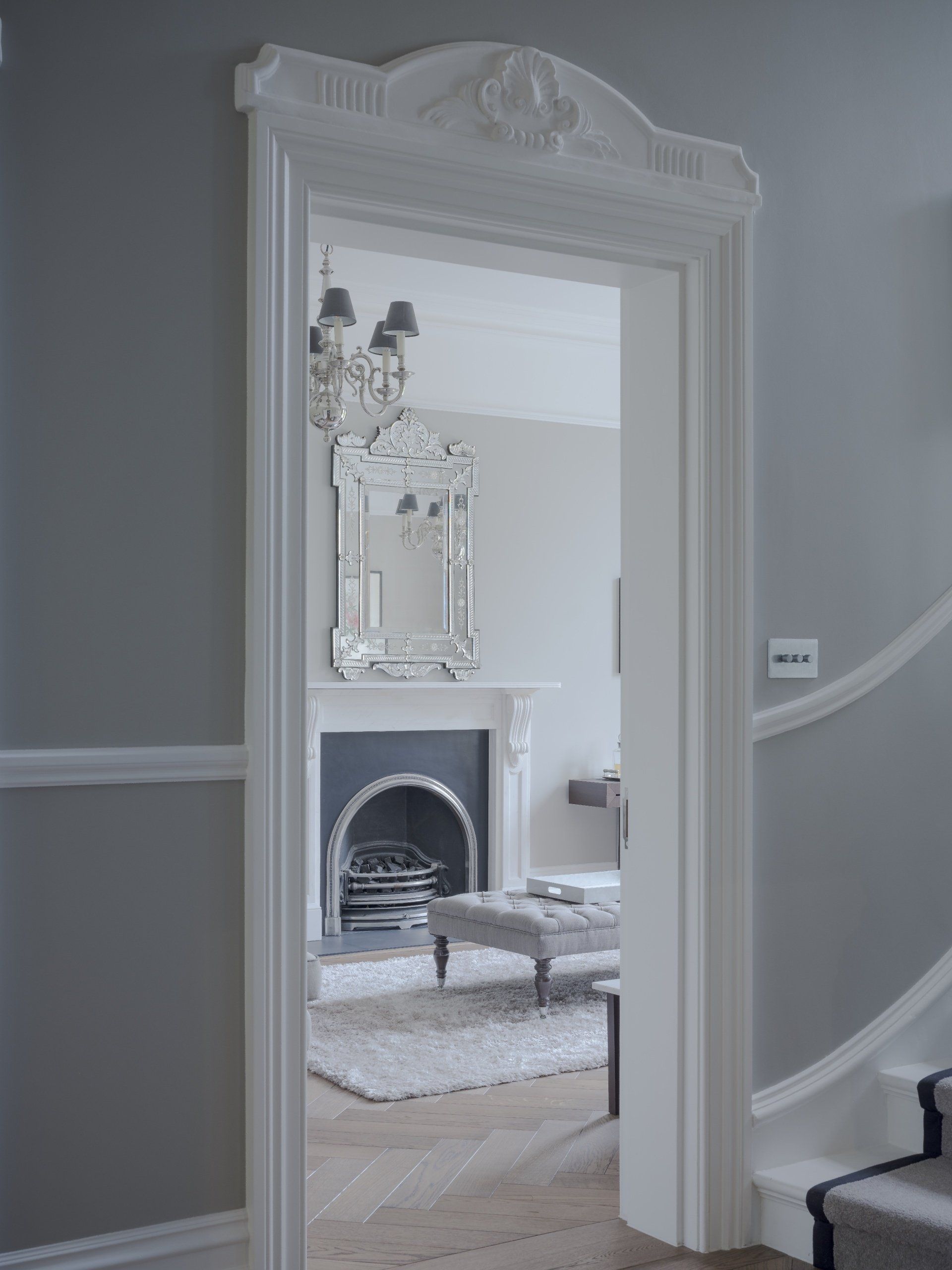 White doorway framing a gray living room with fireplace, mirror, and pale rug