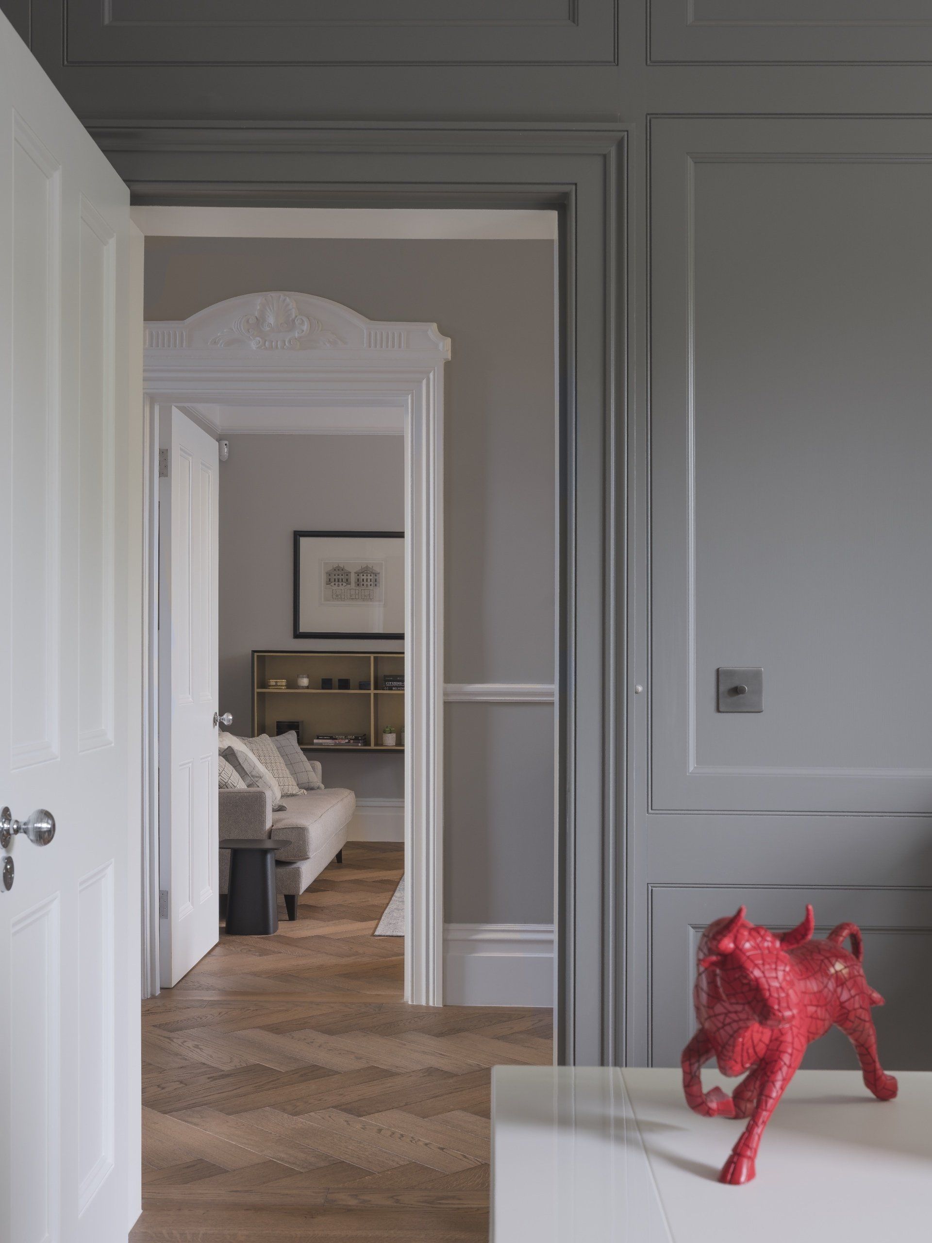 White paneled hallway with open doorway to a bedroom; red statue on a table in the foreground.