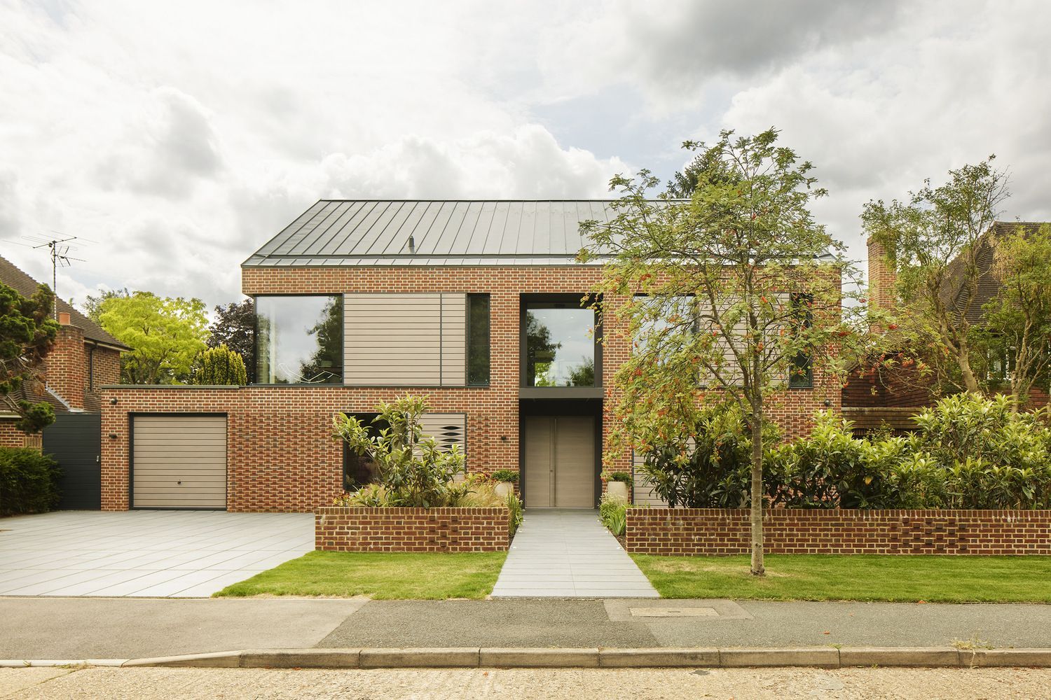 Modern two-story house with brick accents, garage, and front walkway surrounded by trees and greenery