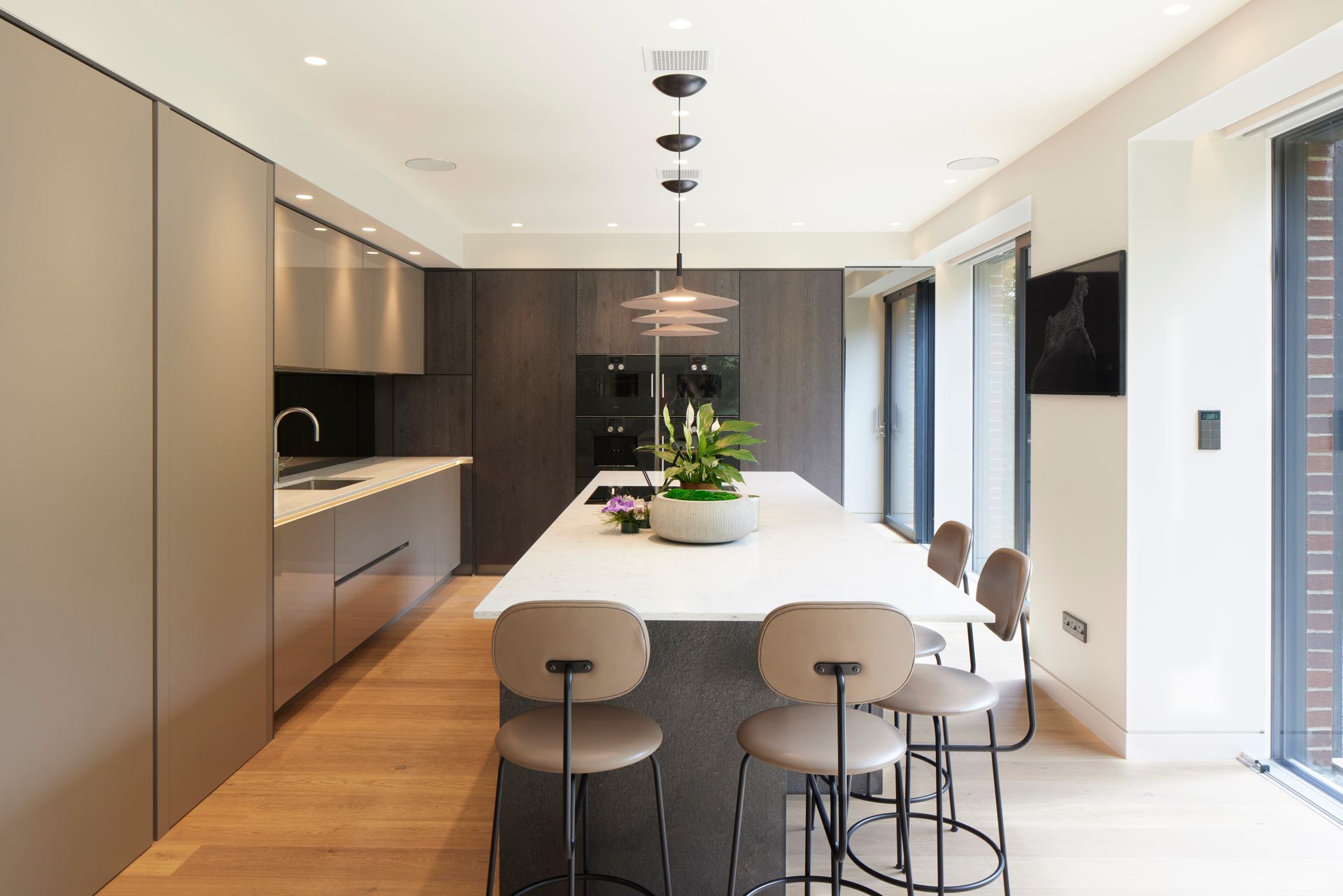 Modern kitchen with dark cabinets, white island, wood floor, and bar stools in a bright open-plan space