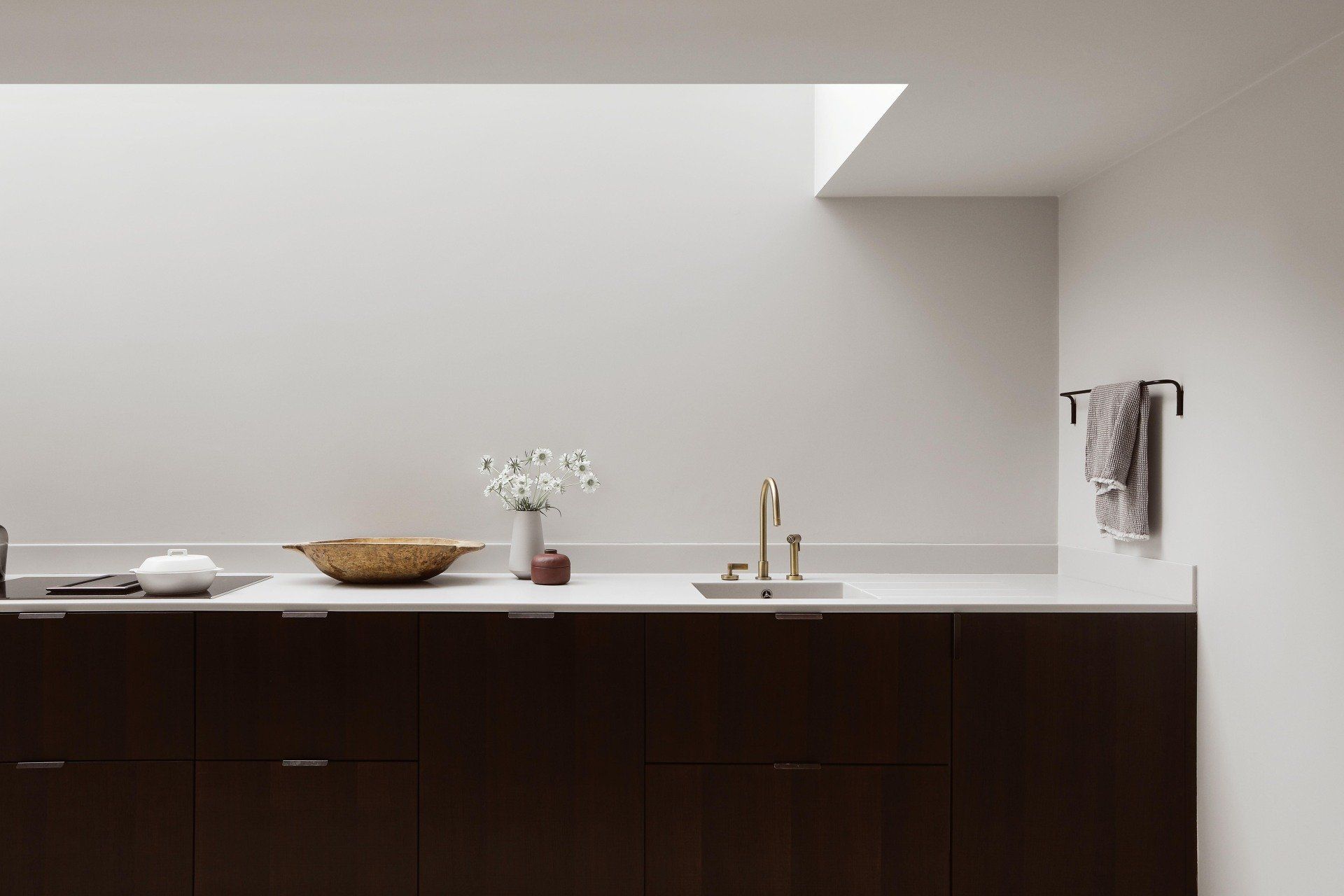 Minimalist bathroom vanity with dark wood cabinets, white countertop, sink, mirror, and towel rack