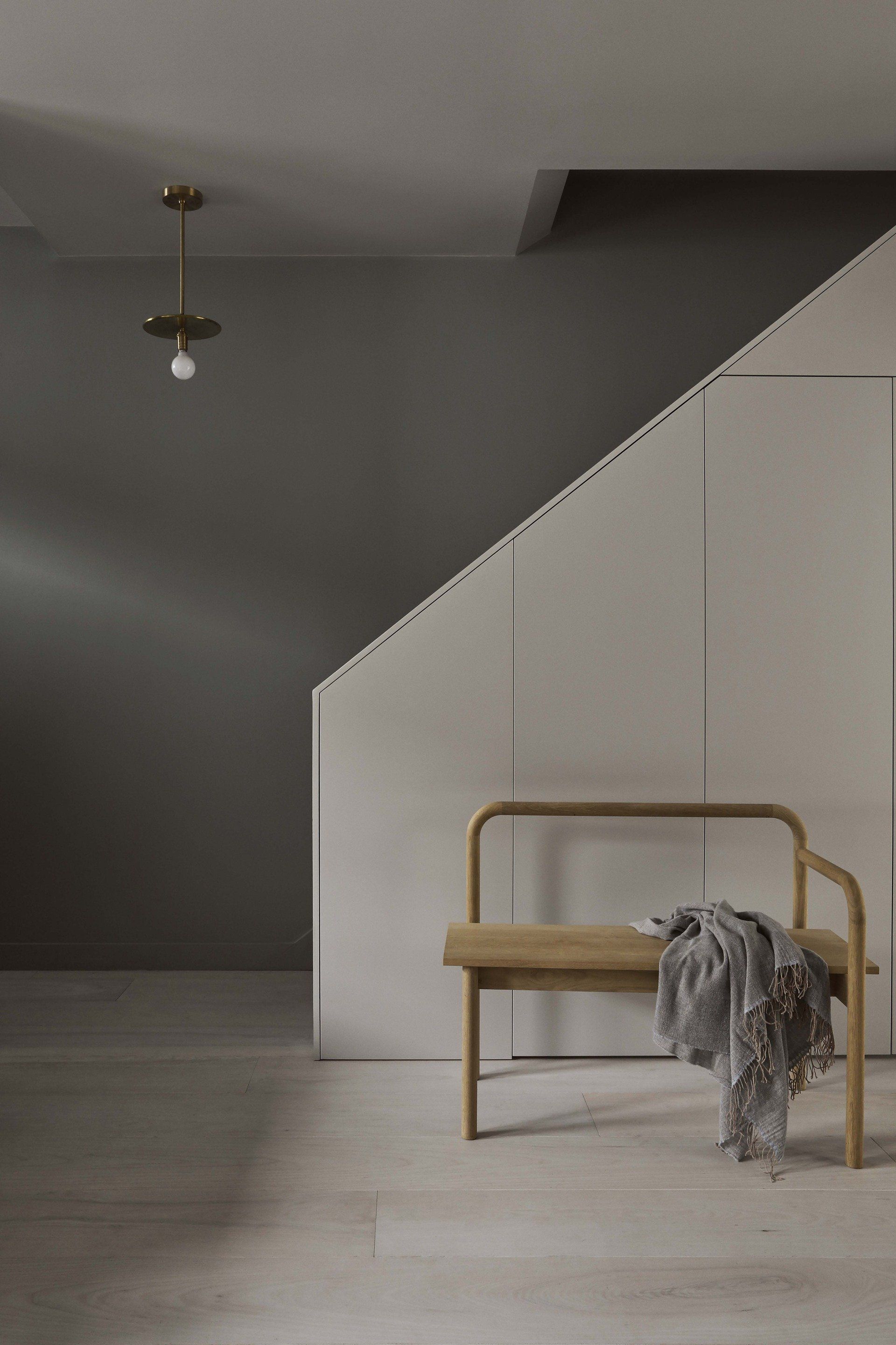 Minimalist room with a wooden bench and draped gray blanket beside a slanted white wall.