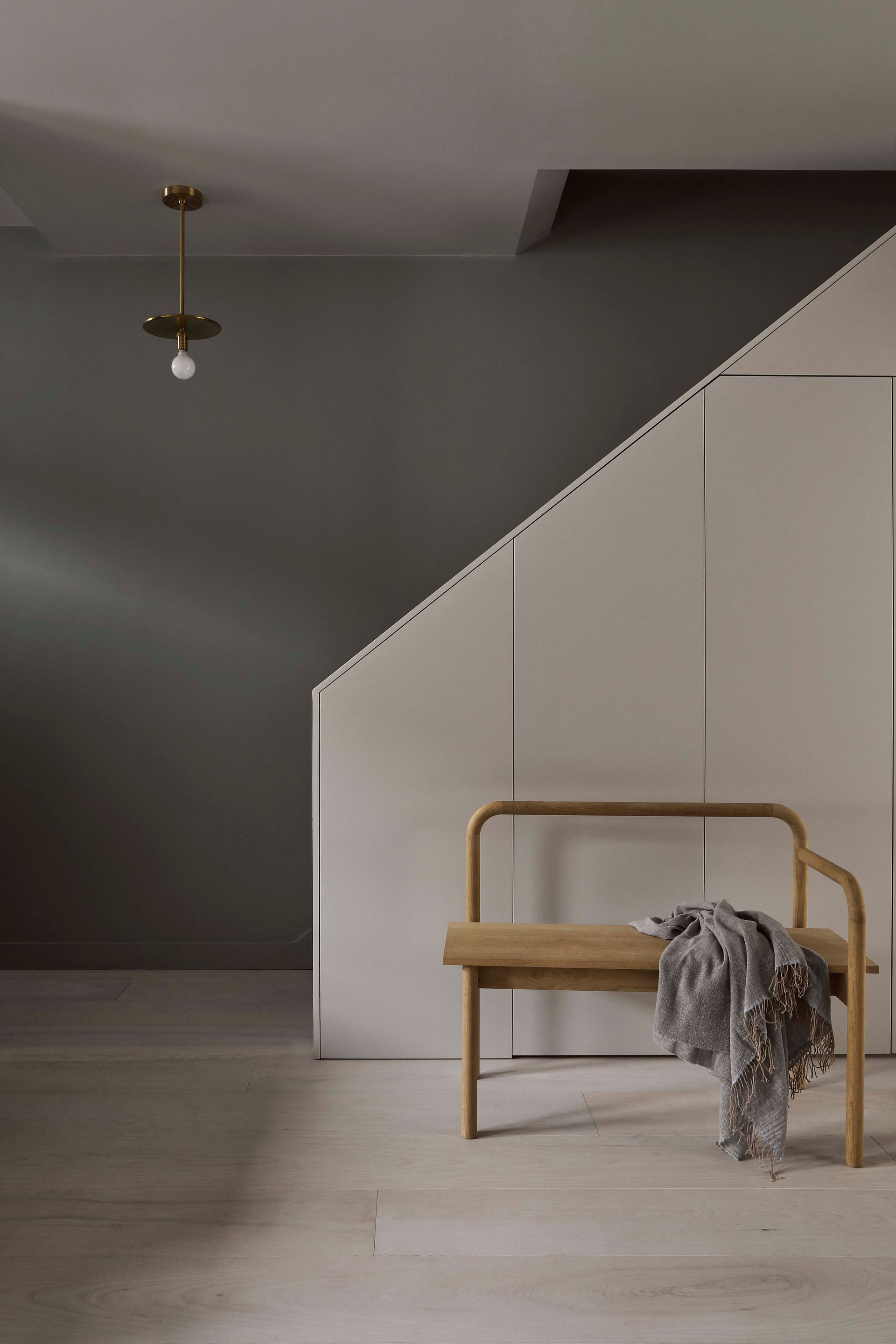 Minimalist room with a wooden bench, gray throw, and white staircase wall