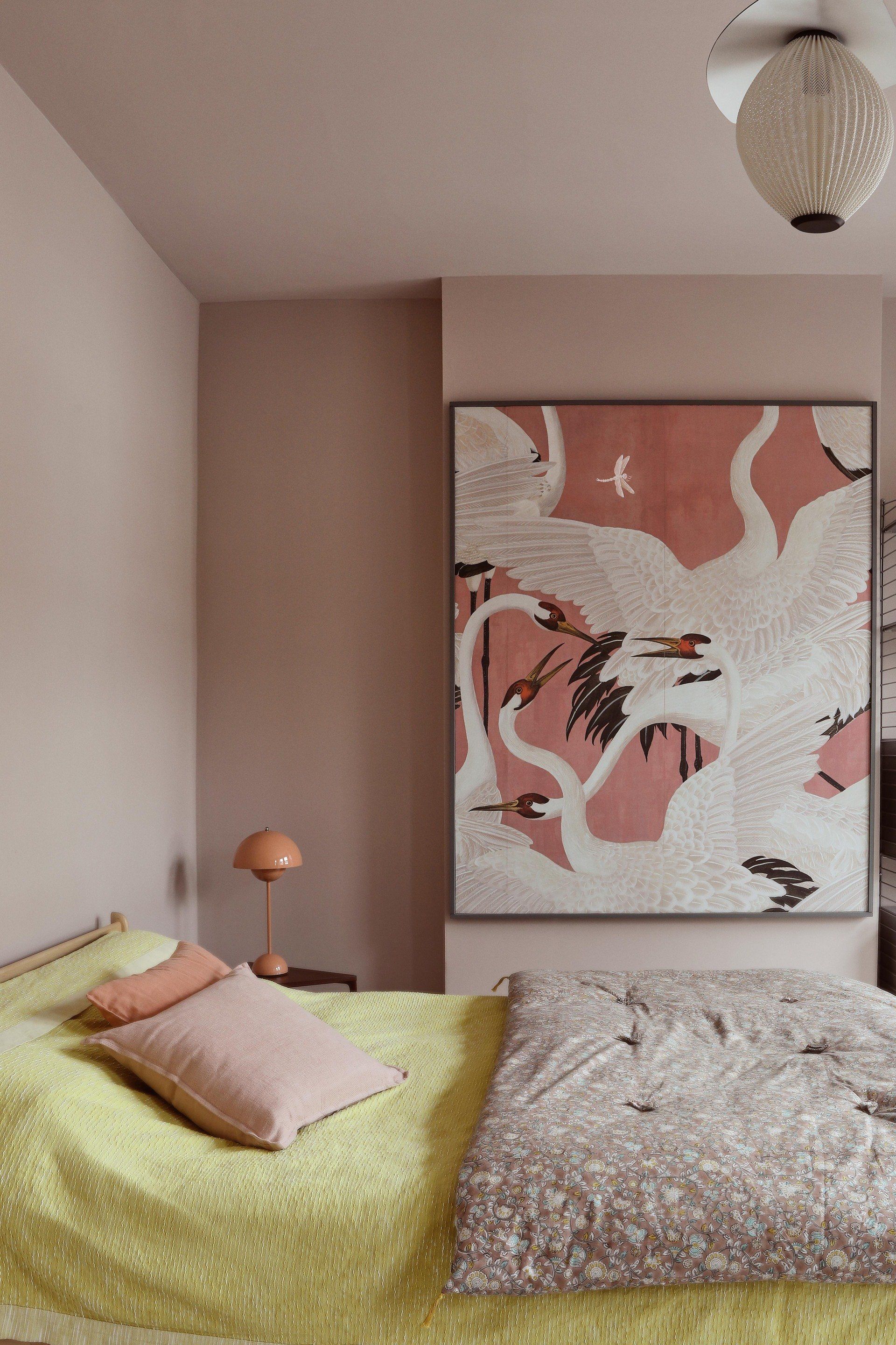 Cozy bedroom with a bed, pink and green bedding, abstract wall art, and a hanging light fixture.