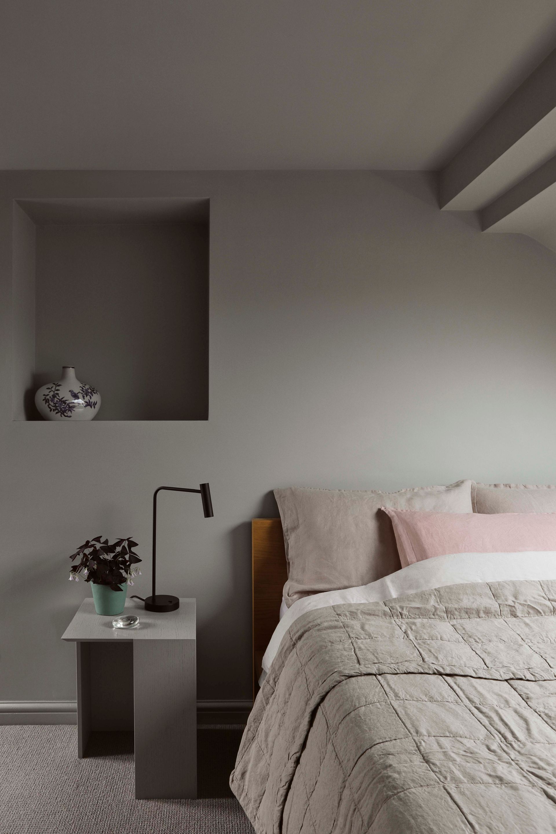 Minimal bedroom with a bed, bedside table, lamp, flowers, and a wall niche with decor