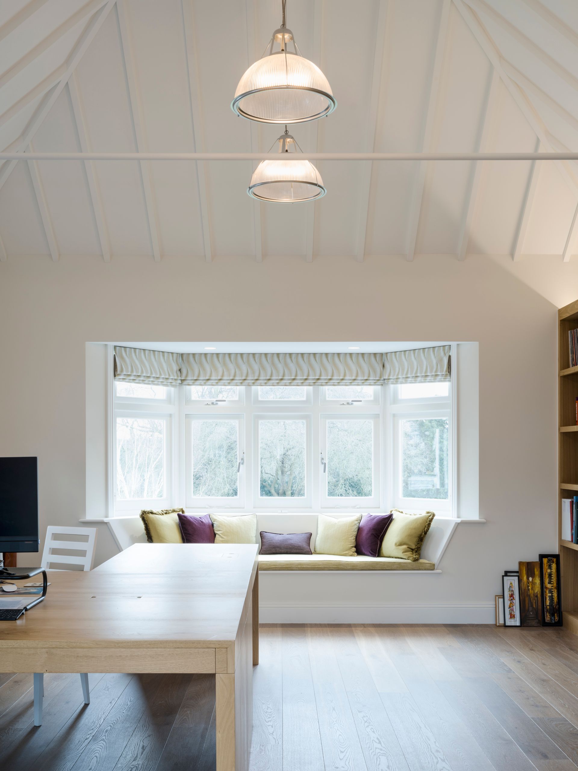 Bright loft living room with large bay window seat, wooden table, and pendant lights