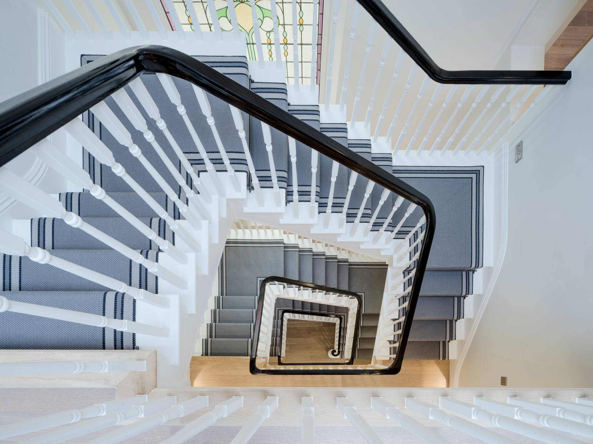 Spiral staircase with white balusters and dark handrails, viewed from above in a bright interior.