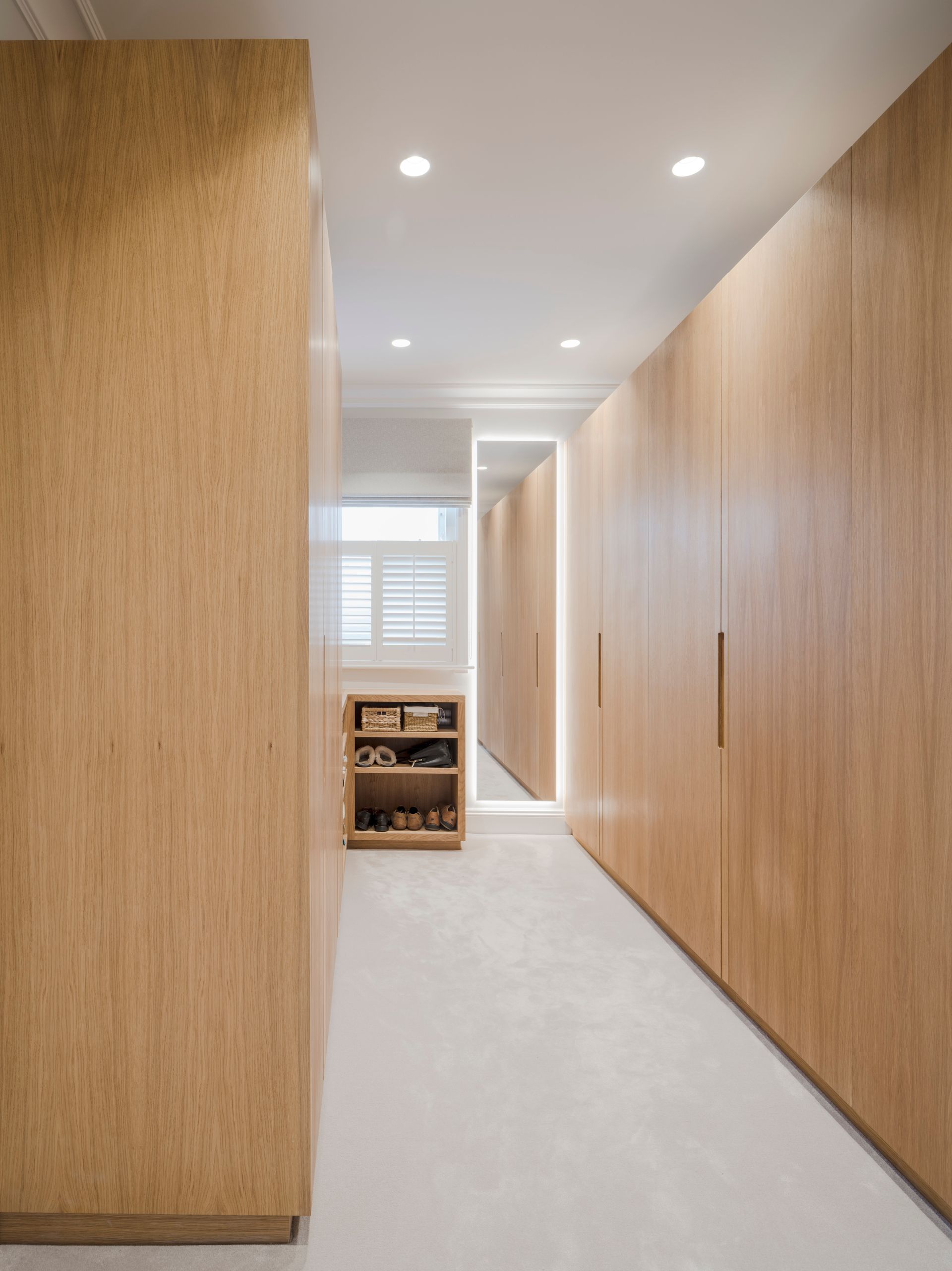 Modern hallway with light wood walls, recessed ceiling lights, and a small cart near the window.