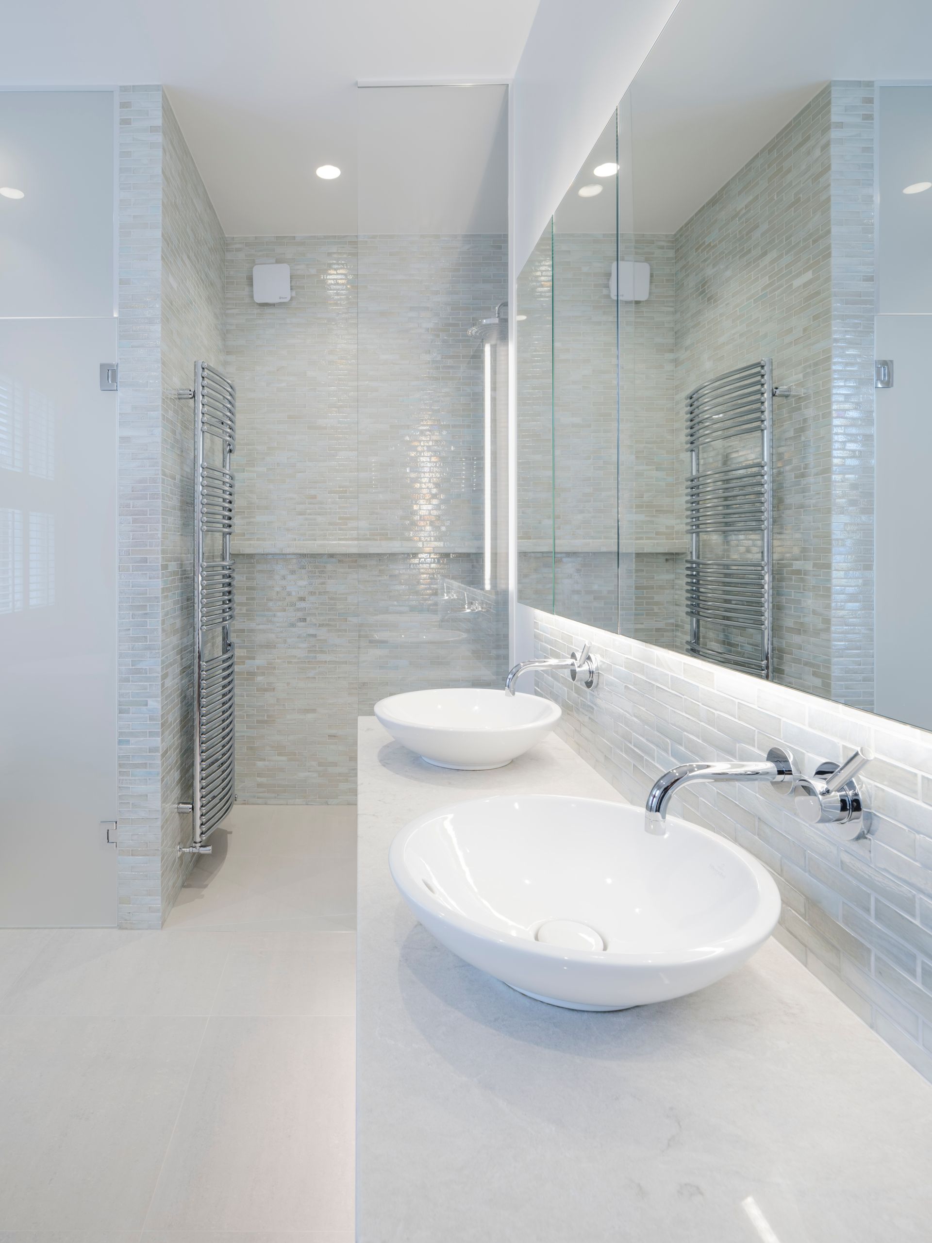 Bright modern bathroom with two white vessel sinks, large mirrors, and glass shower doors