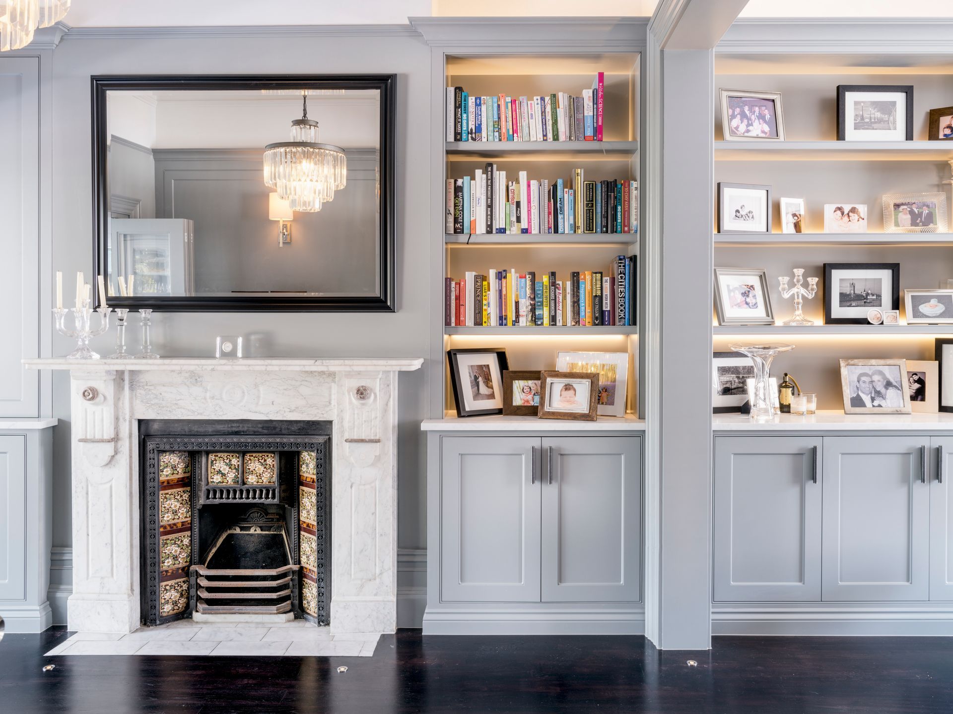 Elegant living room with fireplace, mirror, built-in bookshelves, and framed photos on light gray walls
