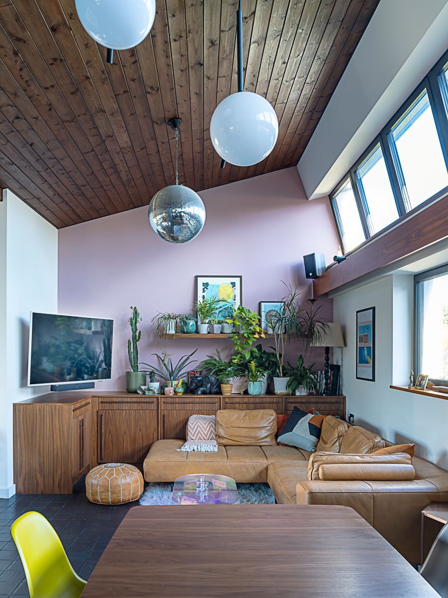 Cozy living room with tan sectional, wooden ceiling, potted plants, TV, and hanging globe lights