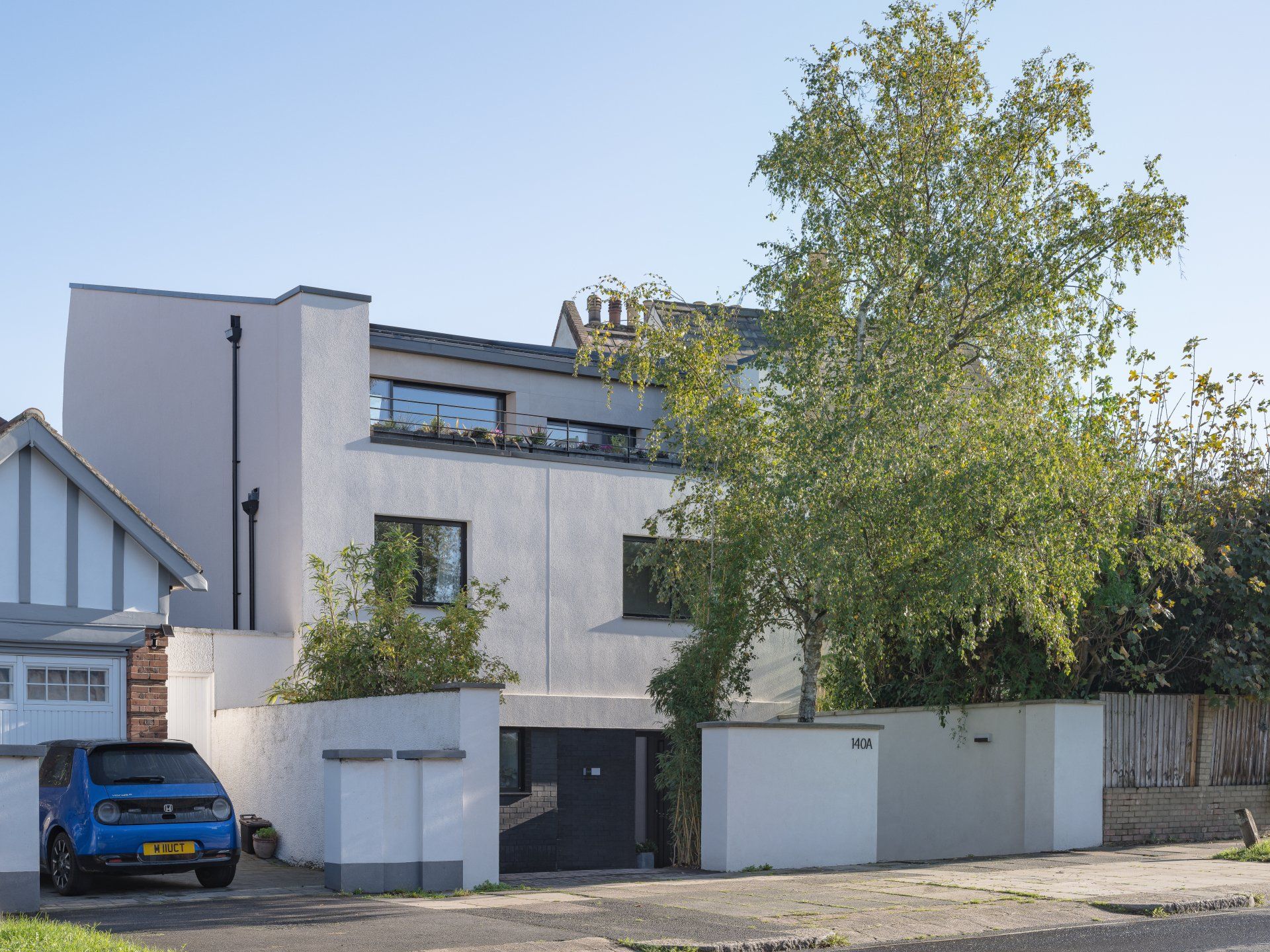 Modern white house with a tall tree and a blue car parked in front