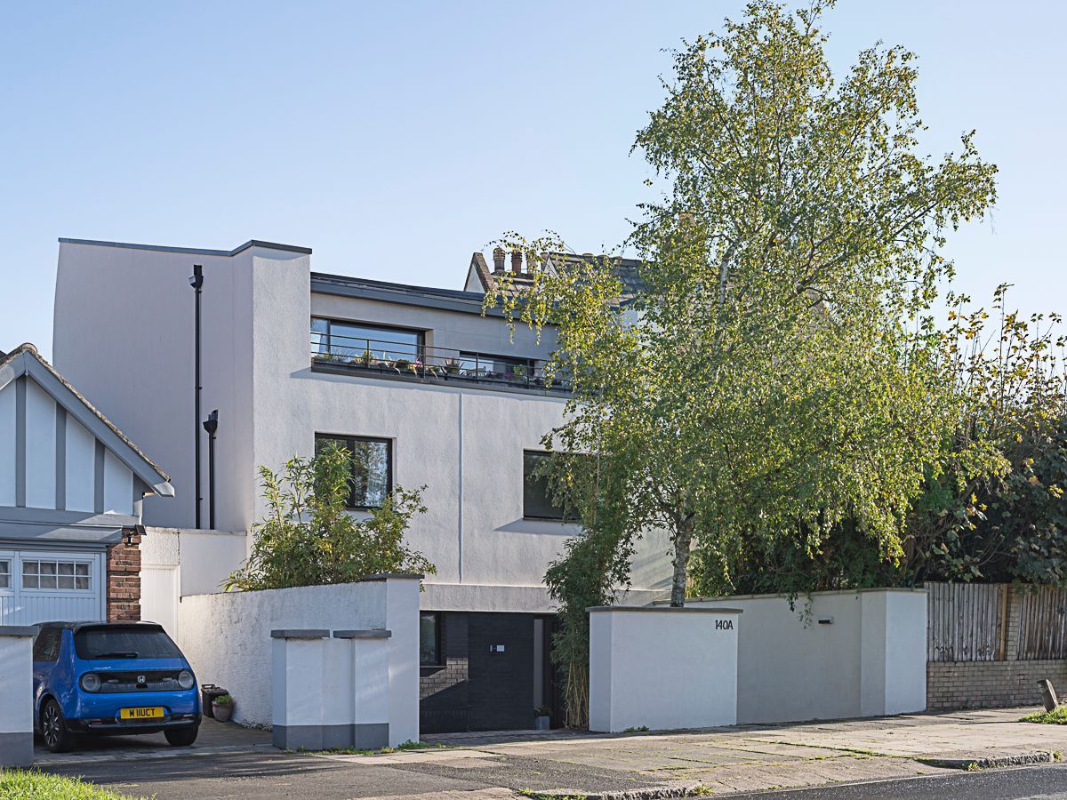 Modern white house with a blue car parked outside and a large tree in front