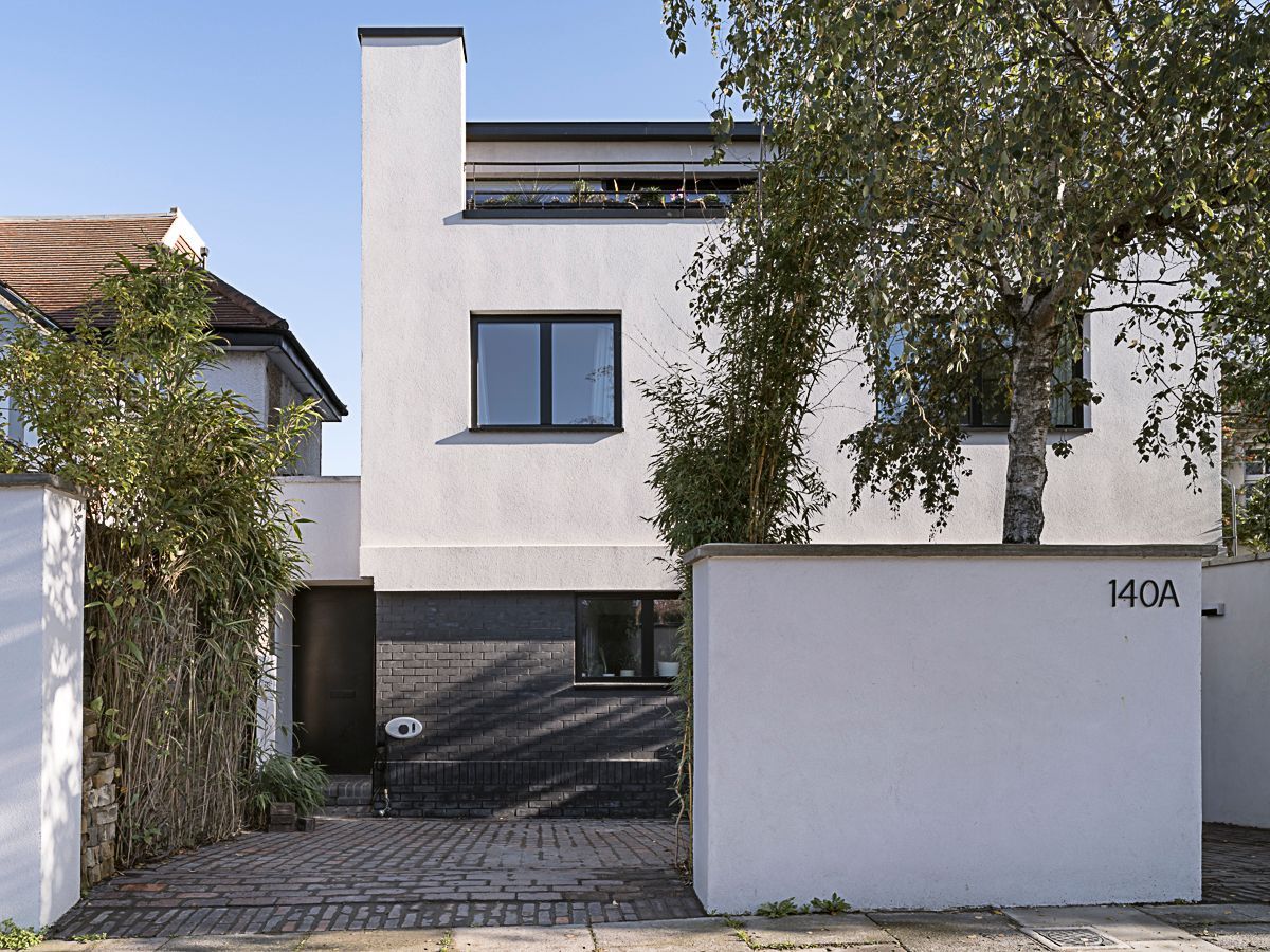 Modern white house with a driveway, gate, and trees in front
