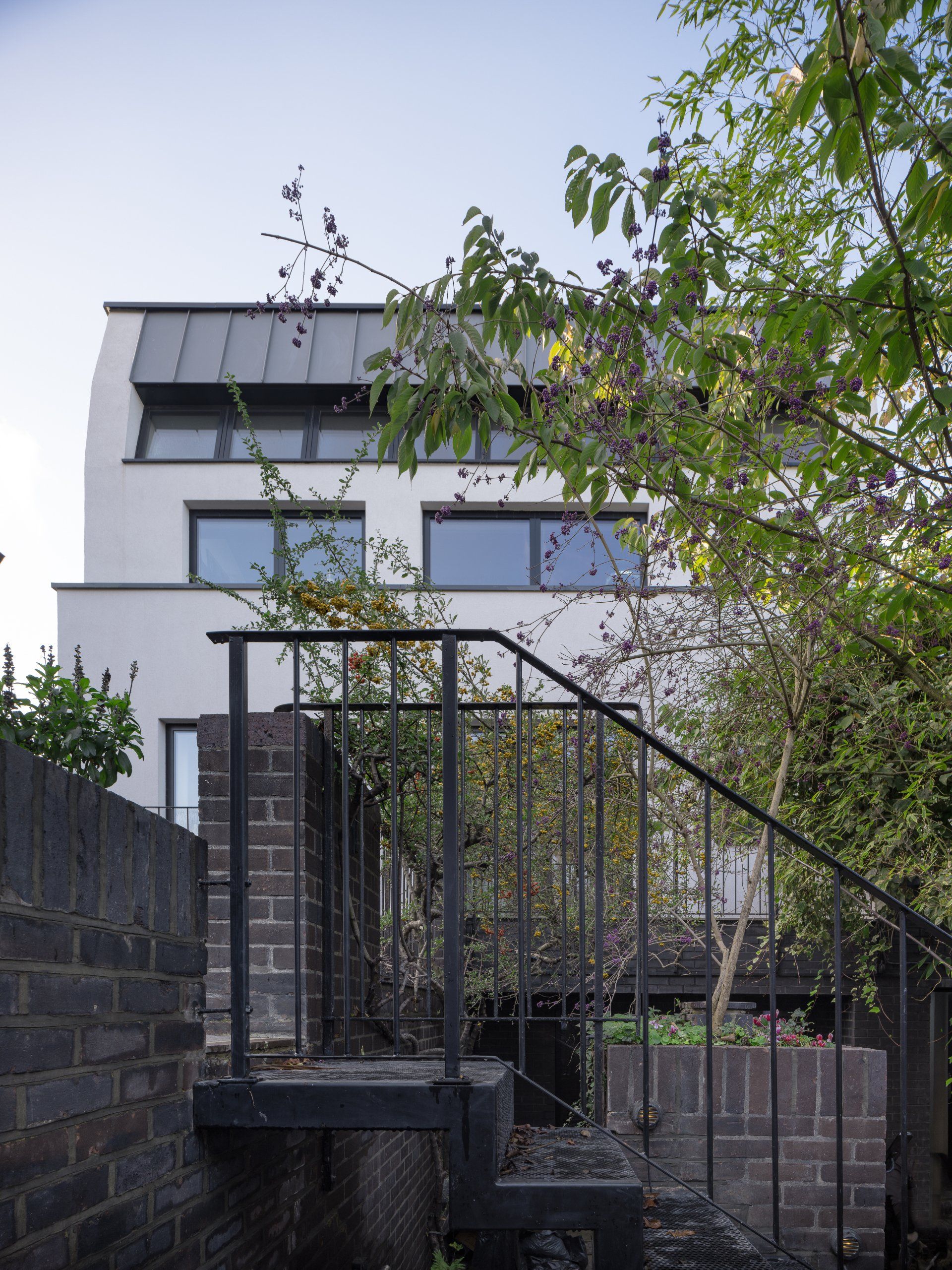 Modern white house with dark windows behind a black metal stair railing and trees