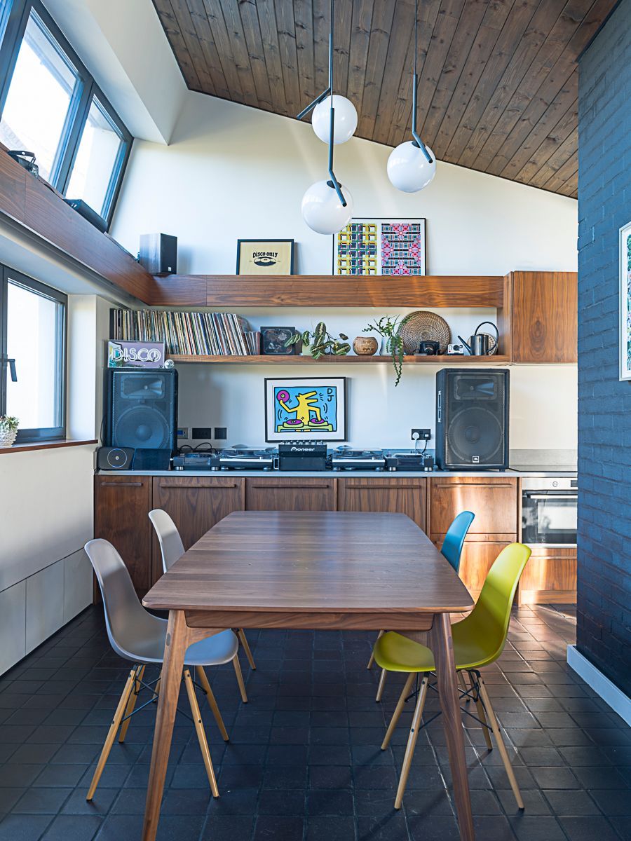 Modern dining room with wood ceiling, table, colorful chairs, and built-in shelves with speakers and TV.