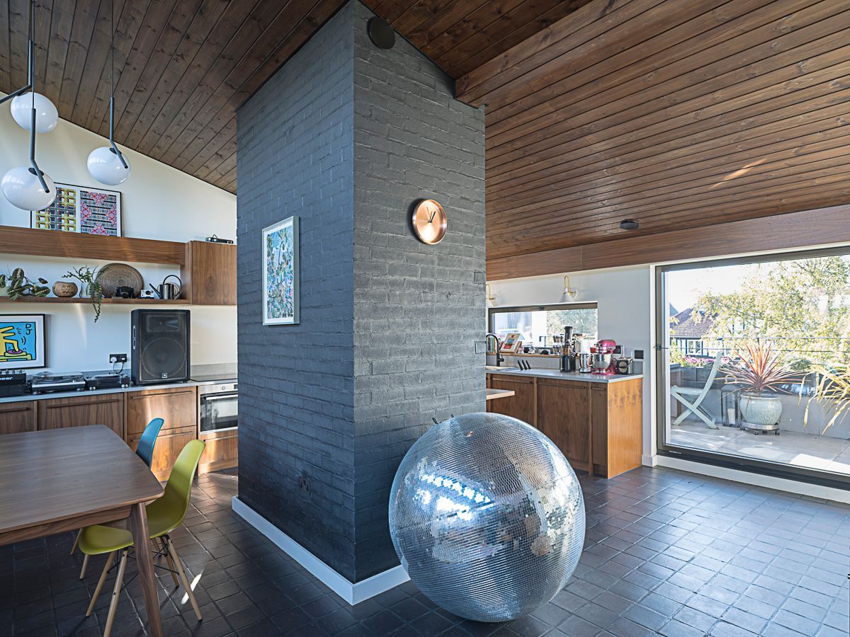 Modern open-plan living room with wood ceiling, central brick column, and large mirrored disco ball