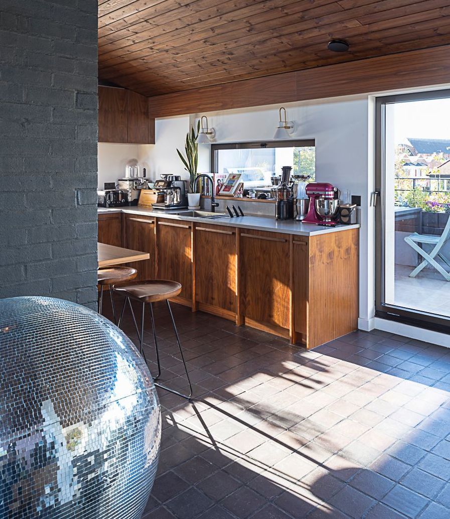 Modern kitchen with wooden cabinets, sunlit counter, and a large mirrored disco ball in the foreground