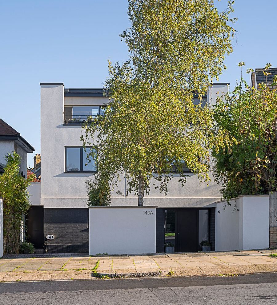 Modern white townhouse behind a large tree, with a sidewalk and street in front