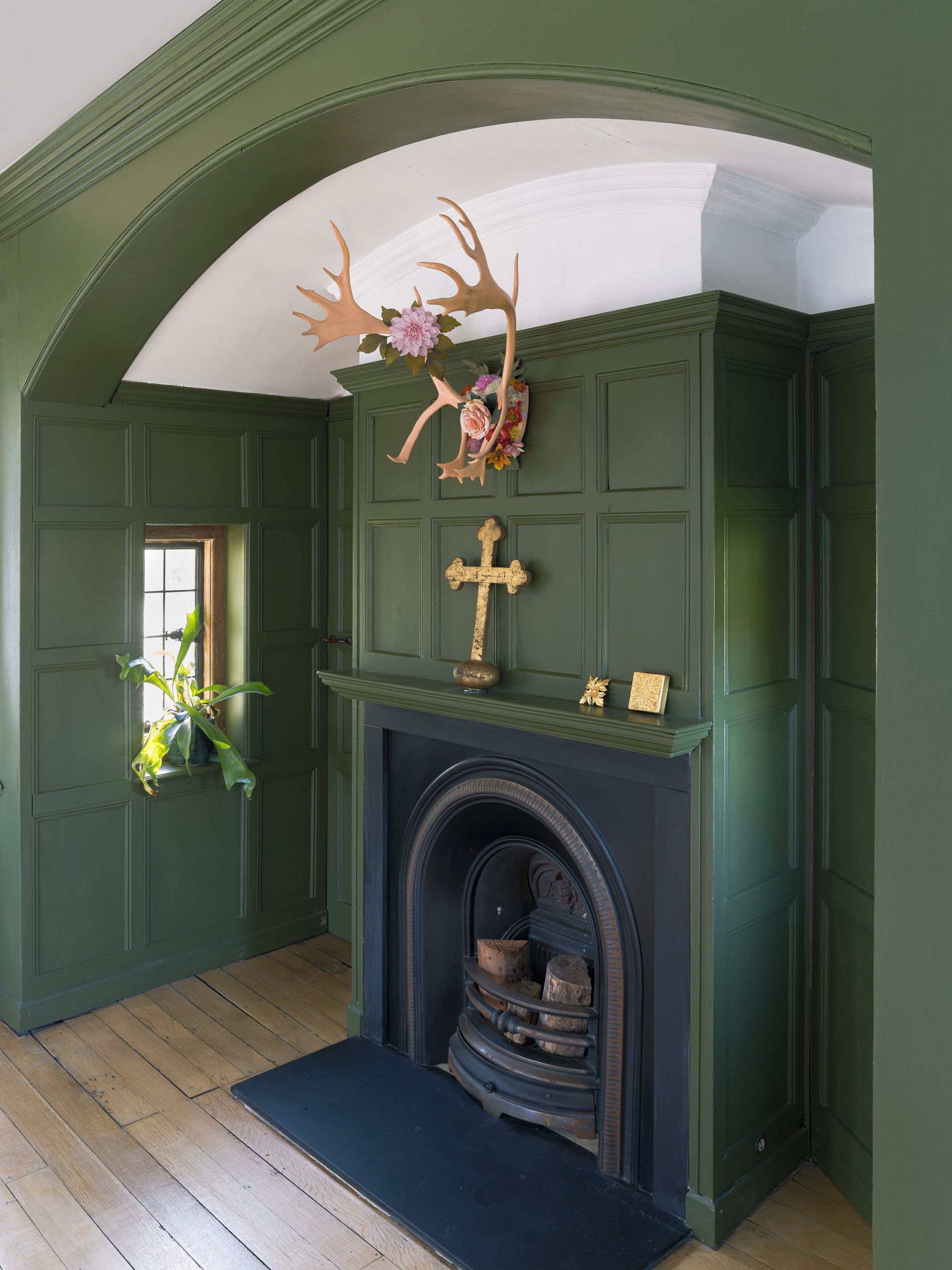 Green-paneled room with arched ceiling, fireplace, and decorative floral arrangement above the mantel
