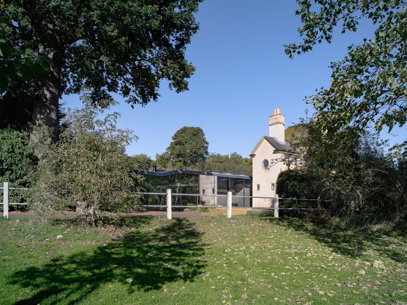 Small white house beside a fenced grassy yard, framed by trees under a clear blue sky.