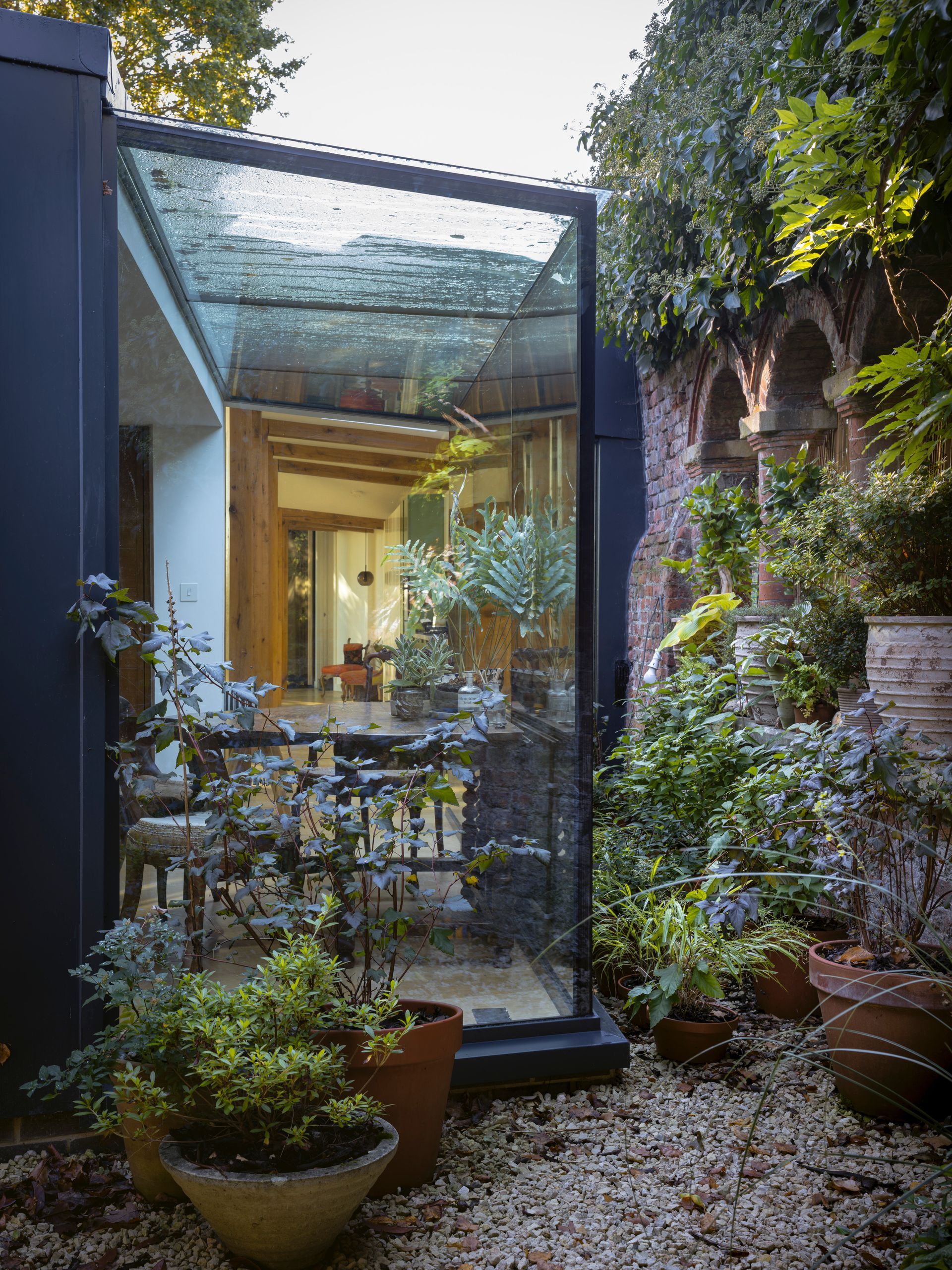 Small courtyard with potted plants and a glass-roofed patio beside a house, lit by warm indoor light