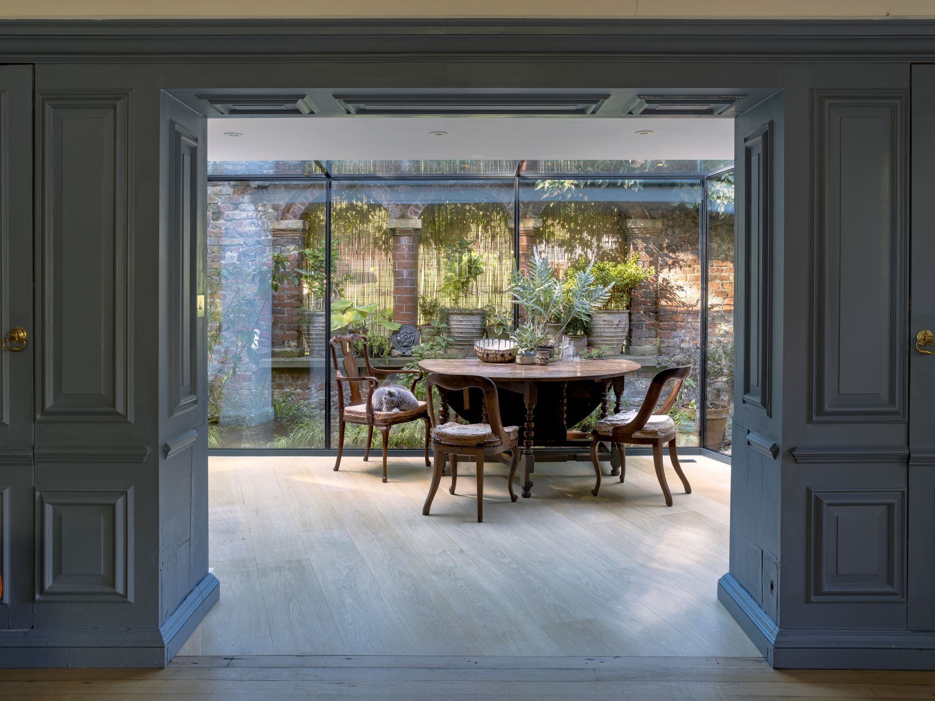 Open French doors to a patio with a wooden table and chairs in a bright garden courtyard