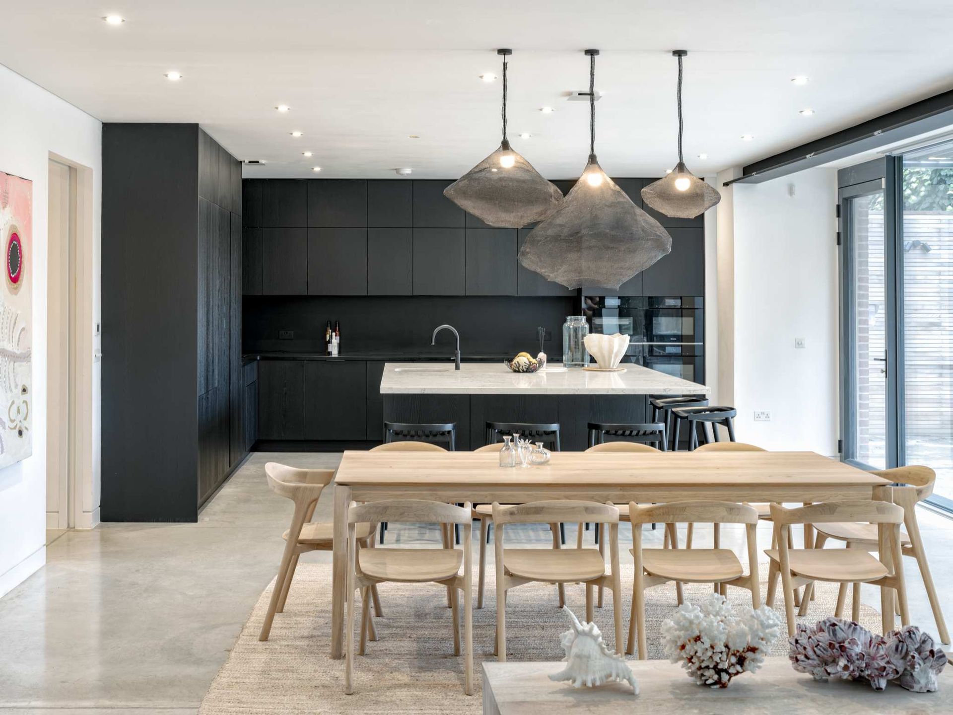 Modern dining room with wooden table, black kitchen cabinets, pendant lights, and floor-to-ceiling windows