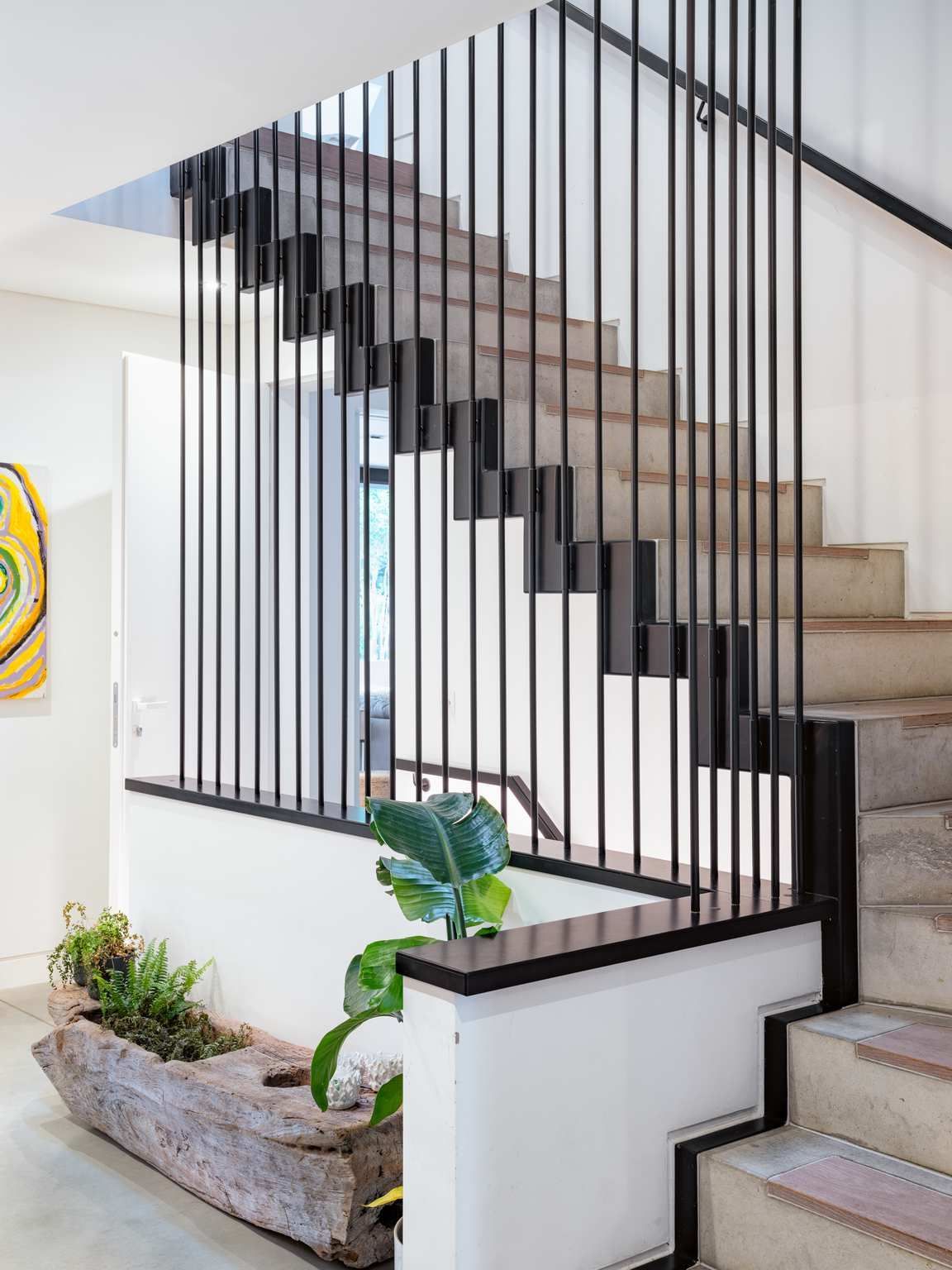 Modern staircase with black vertical railings, white walls, and a small indoor planter below.