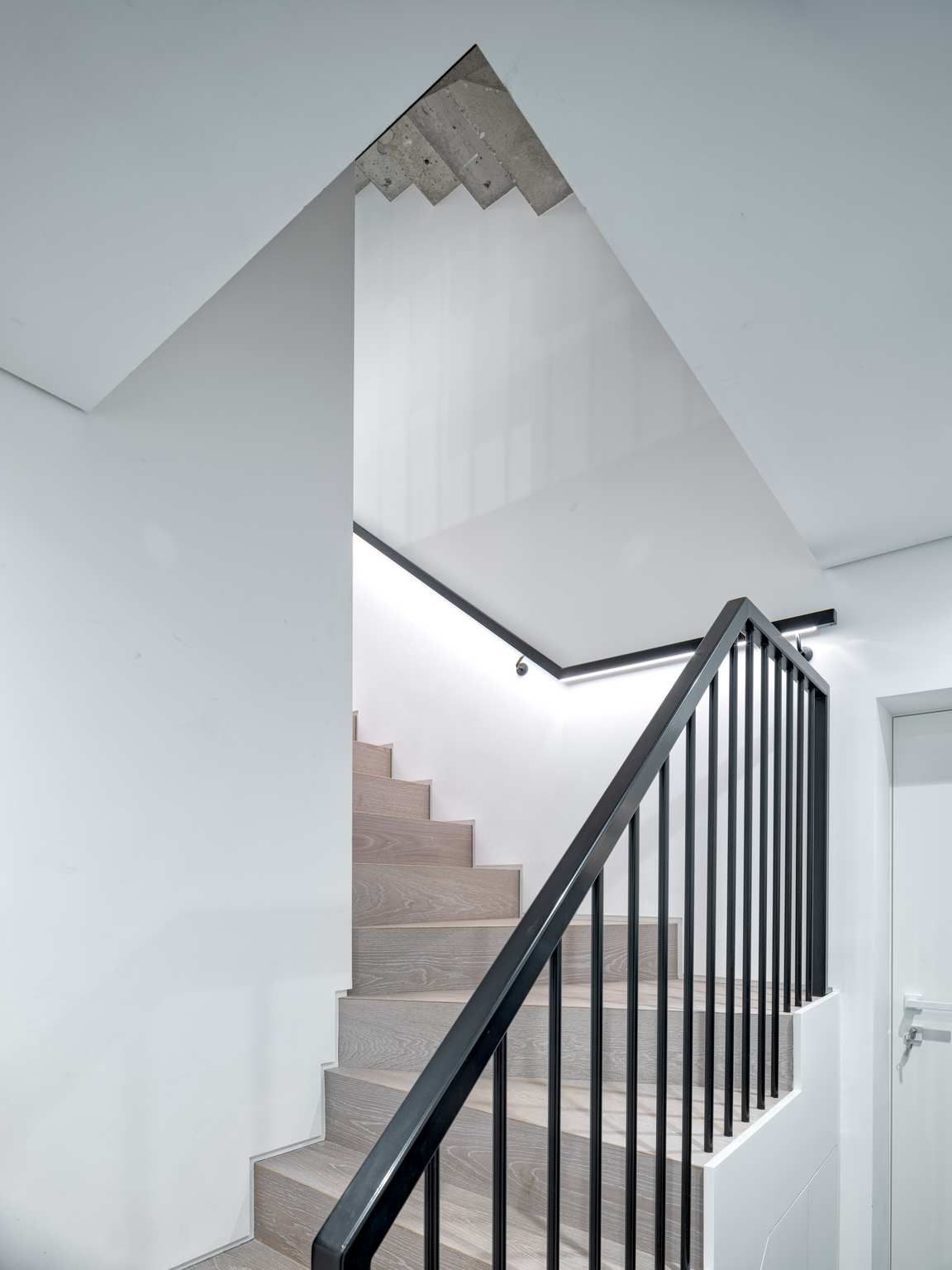 Indoor staircase with beige steps, white walls, and black railing leading to an upper landing