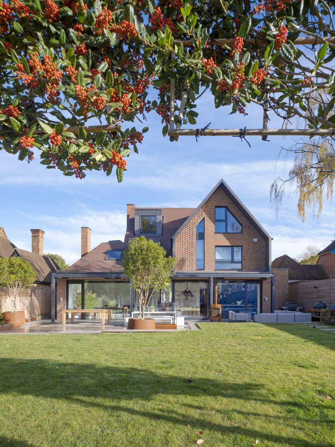 Large brick house with a lawn, patio, and blooming tree branches overhead under a clear blue sky